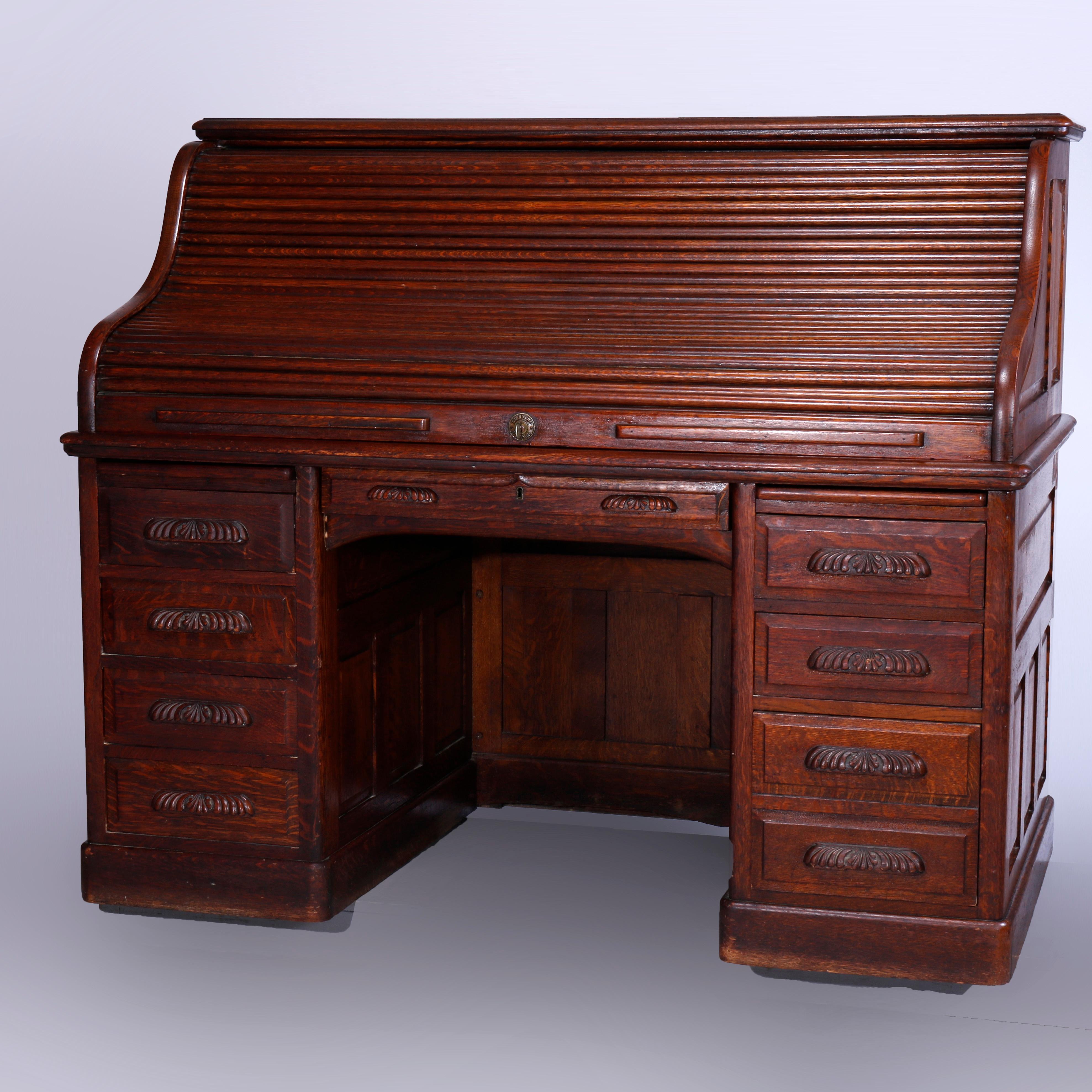 An antique and large desk offers raised panel quarter sawn oak construction with s-roll top opening to full interior with drawers and slots over single central drawer with flanking drawer towers having foliate carved pulls, c1900

Measures-