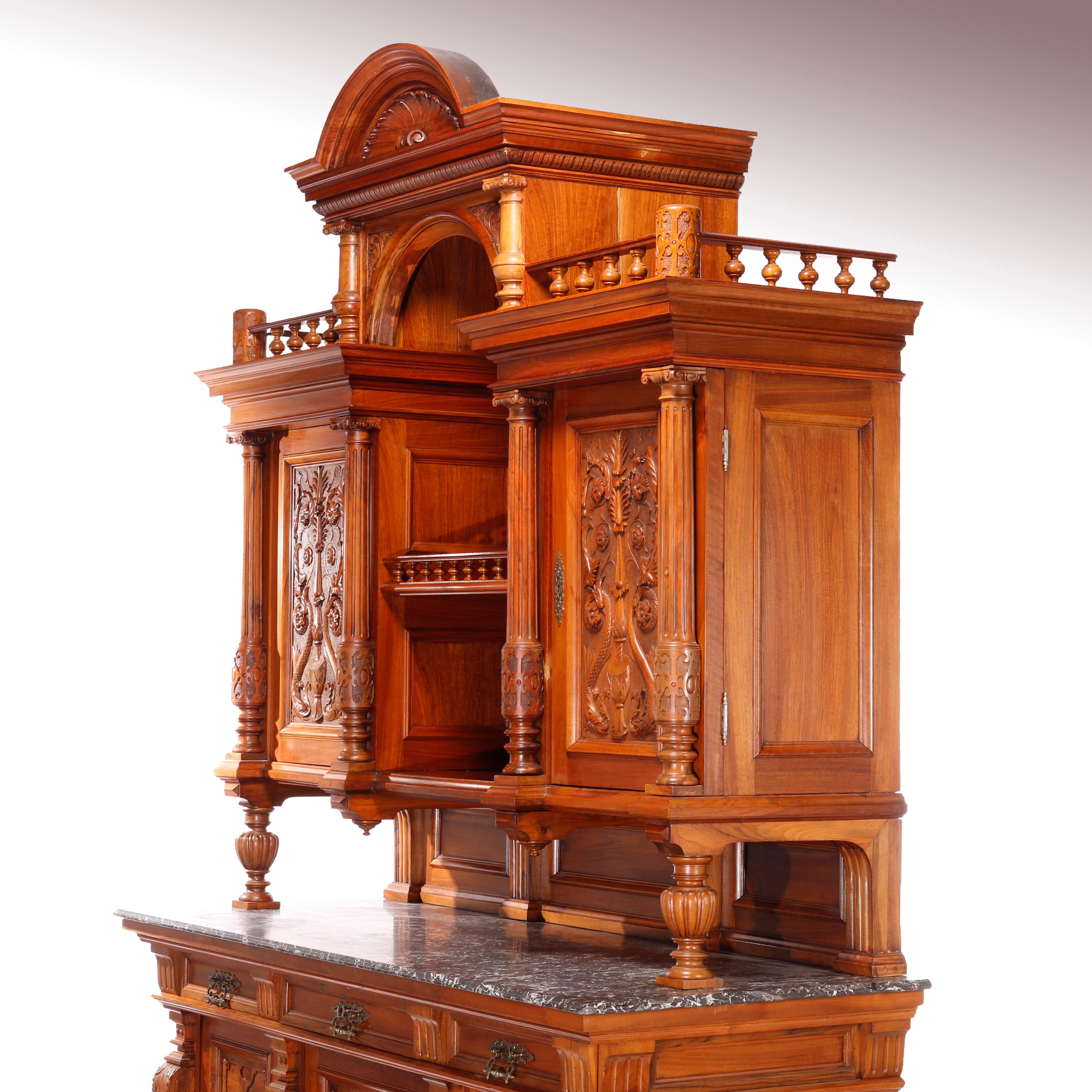 An antique and large hunt board offers walnut and rosewood construction with arched crest over central open tower with flanking blind cabinets having doors with carved foliate and scroll reserves and flanking Corinthian columns and raised on