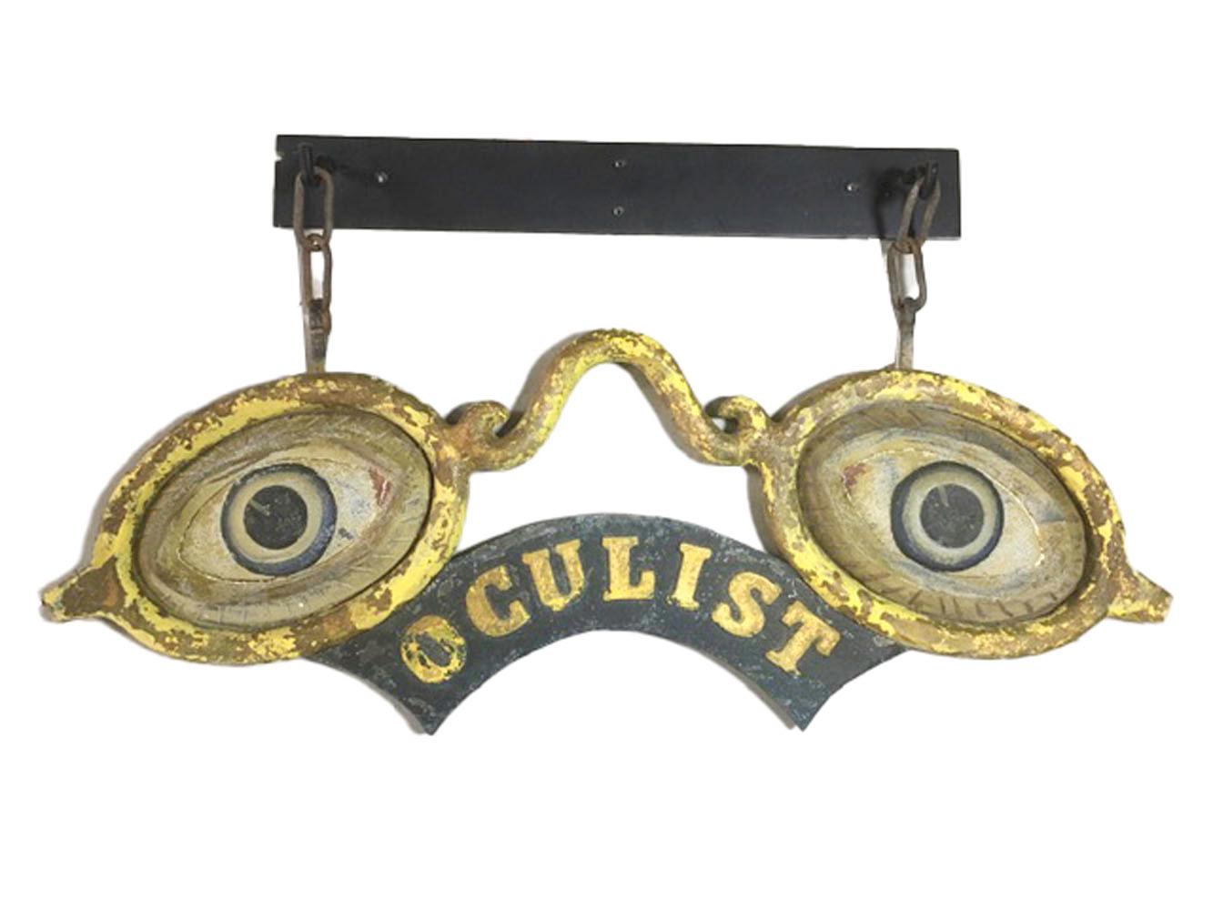 Antique cast iron and zinc trade sign in the form of a pair of gilded cast iron spectacles with painted cast zinc eyes above an arched banner reading 