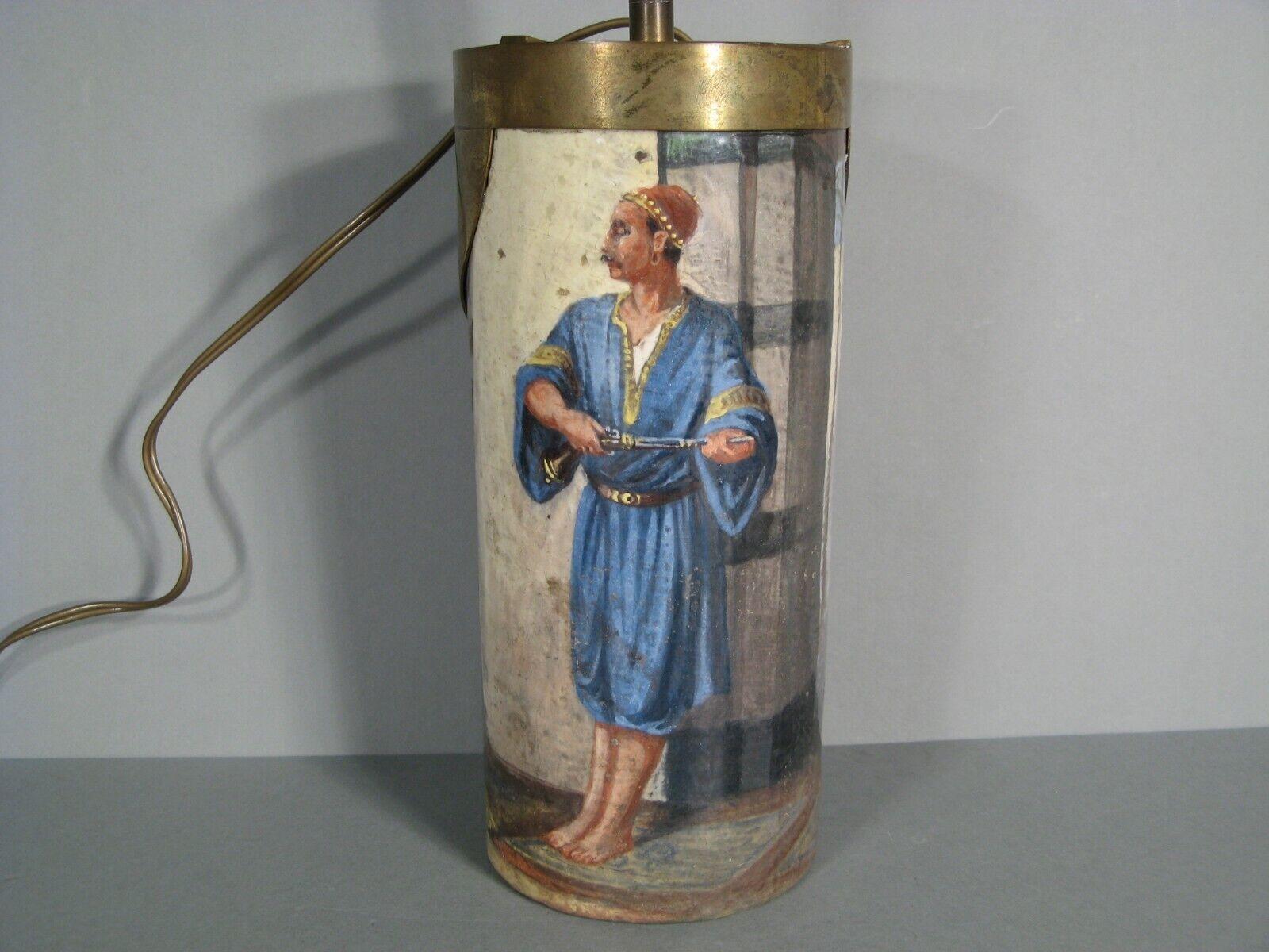 Un vase antique, fabriqué en céramique peinte et émaillée, transformé par la suite en lampe. Le vase présente une scène orientaliste originale représentant un homme armé en tunique bleue attendant au coin d'une rue. Il est monté avec des raccords en