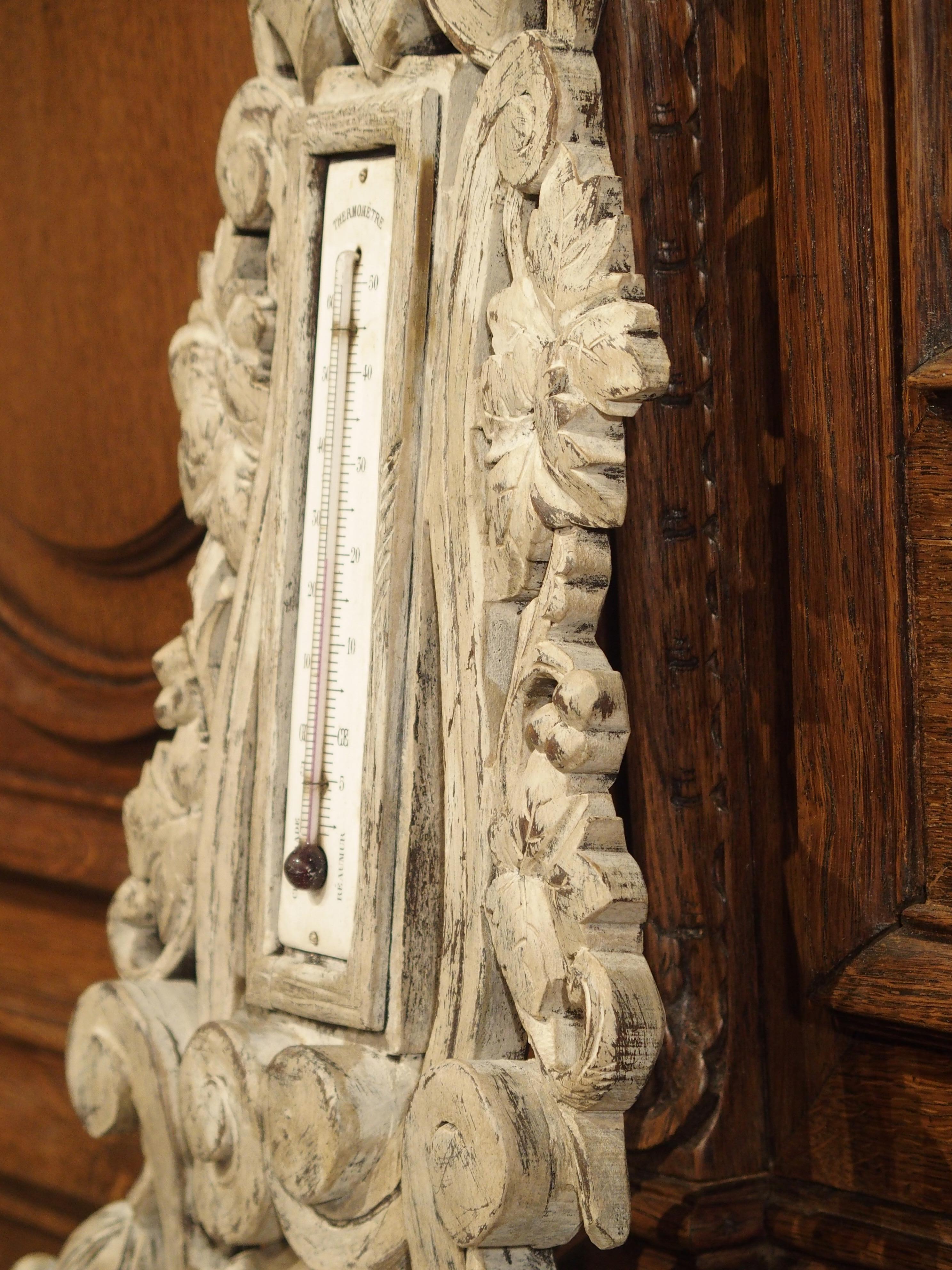 This elegant painted barometer was carved in the late 1800s. The upper portion houses a temperature gauge. The carved decorations include floral and foliate motifs, finials, and a cartouche at the top. The distressed painted finish that was given to