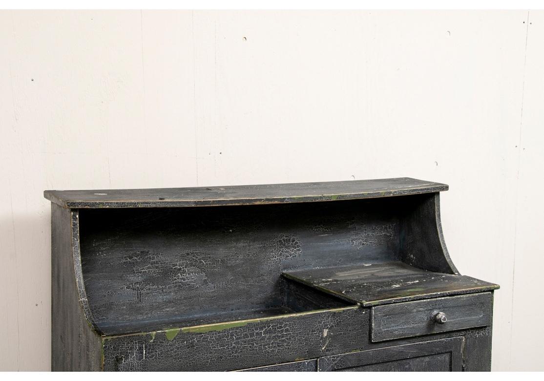 Painted wood in an overall old crackled and worn black paint over a worn green and gilt base paint. The cabinet with sloping sides for the top section. The cabinet right side with a drawer and a dry sink on the left. Below are double doors opening
