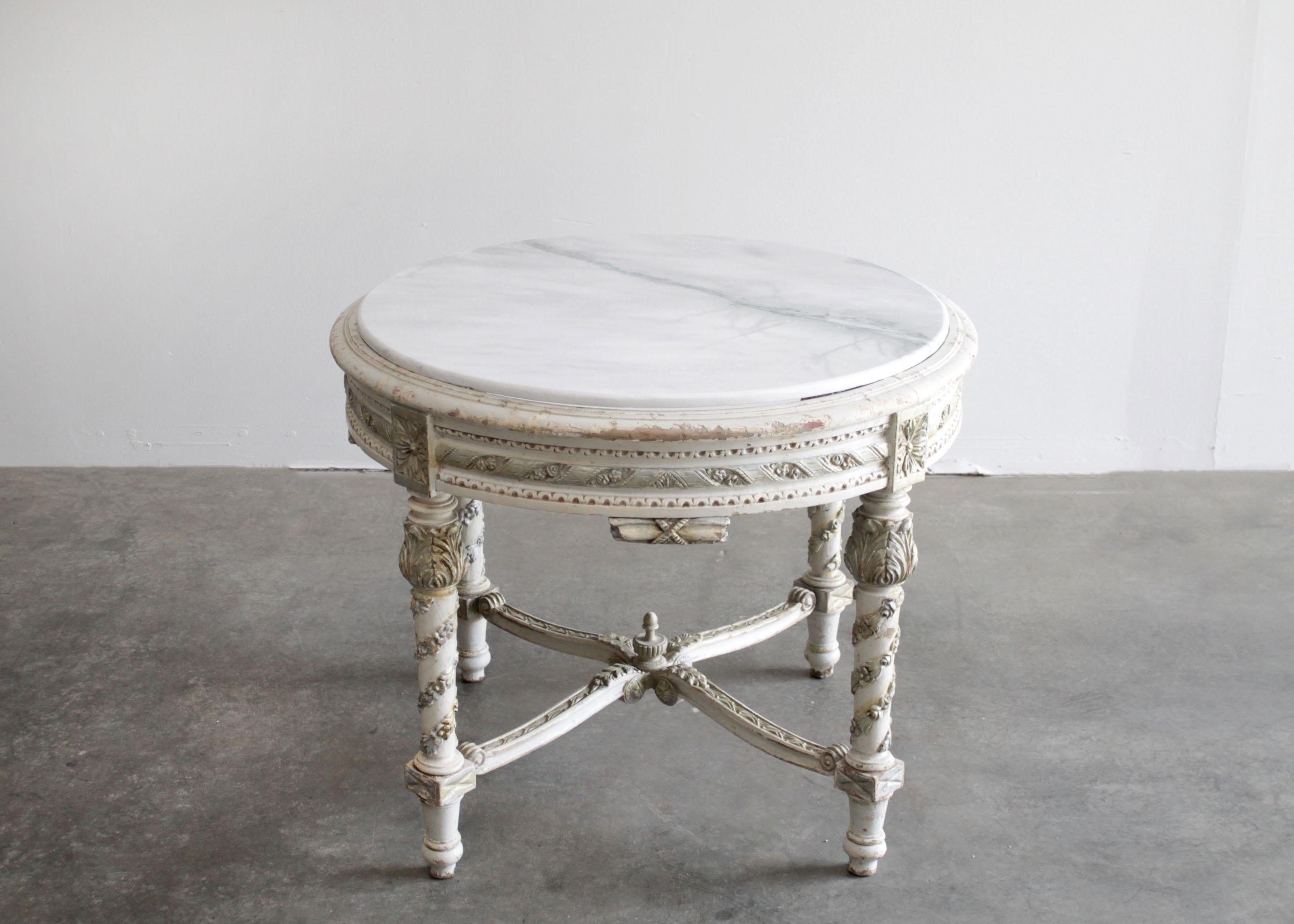 Antique painted French style center table in the Louis XVI style with marble top
This round center table features carved rose garlands around the legs, with a beautiful
carved stretcher and finial.
The marble is a new addition to this table, in a