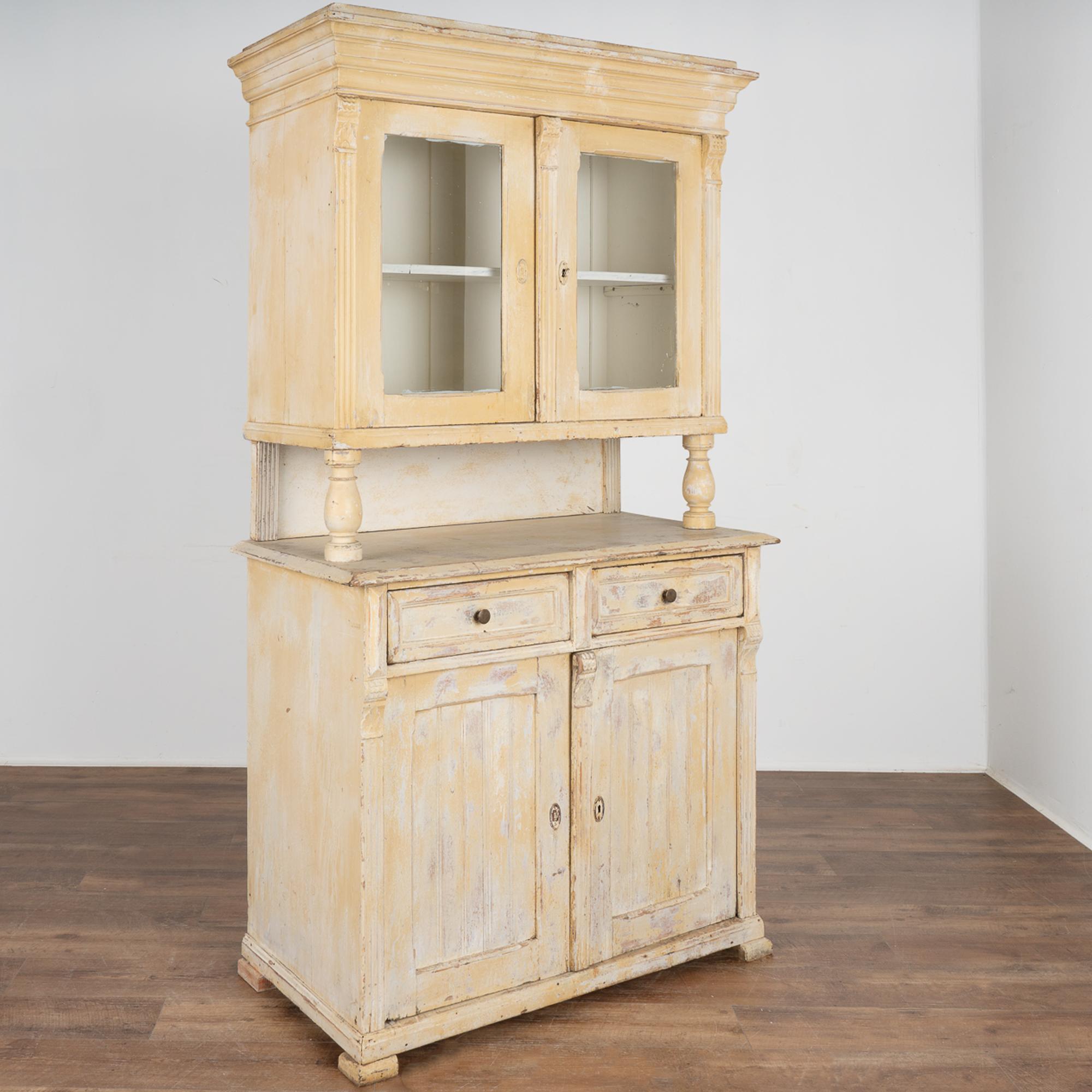 This old pine cupboard has been painted over multiple times in its long life, with current tones of layered pale ochre and white all distressed revealing the natural pine below.
This traditional pine cabinet allows for items to be displayed behind