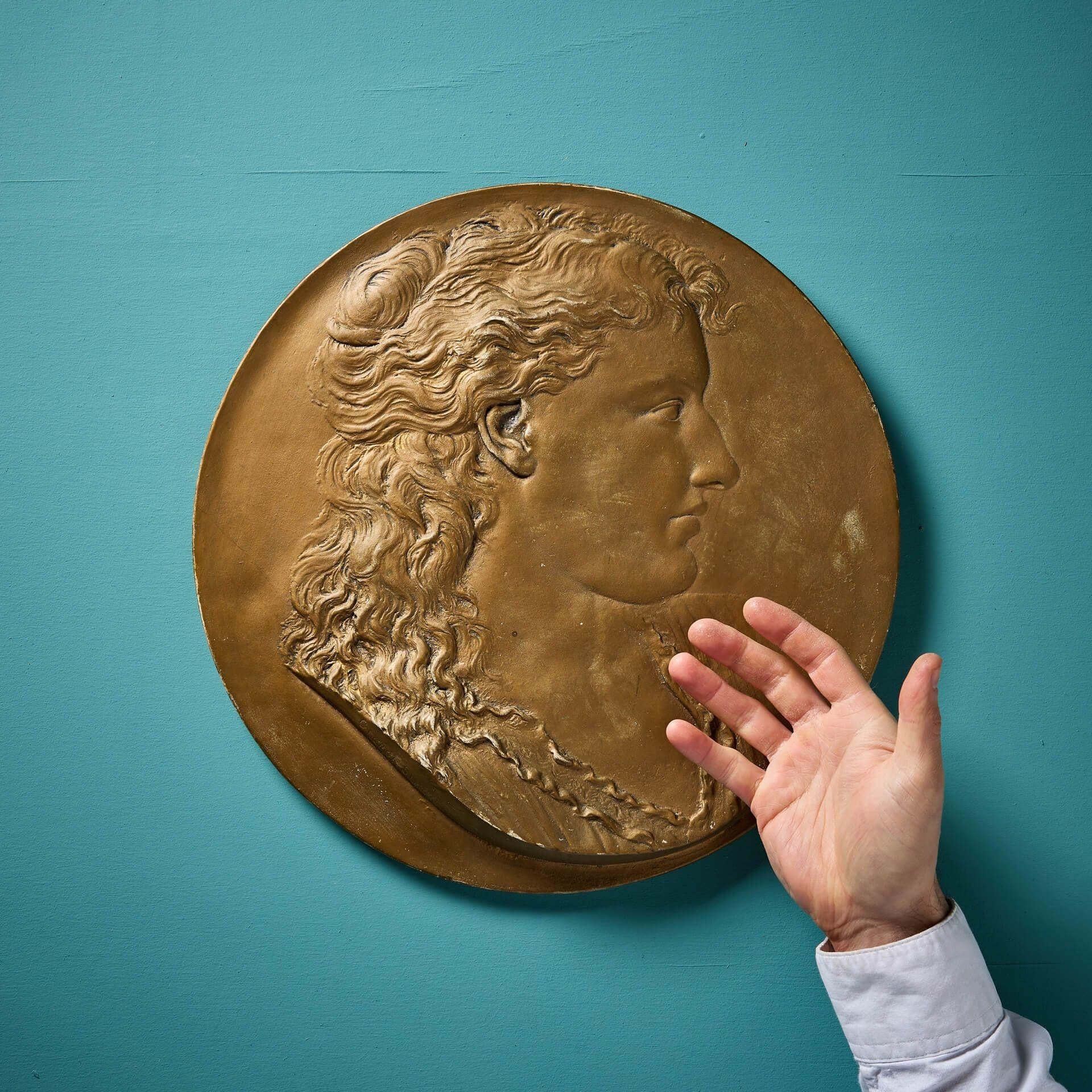 Ein antikes, aus Gips gemaltes Porträt-Rundbild einer Frau im Profil von George Blackall Simonds (signiert).

Dieses dekorative Wand-Rondell ist mit Goldfarbe bemalt und auf der Rückseite mit einem Wandhaken versehen. Es trägt die Inschrift 