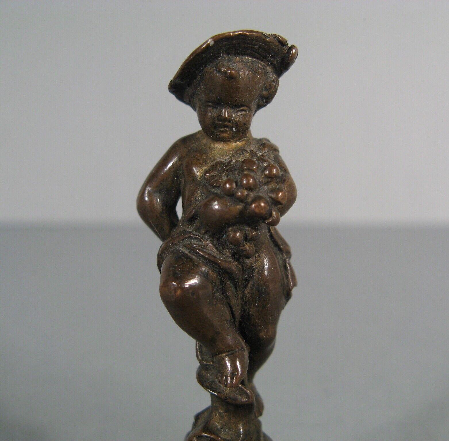 Añade un toque de encanto histórico a tu colección con este raro sello de bronce antiguo. Representando a un querubín vendimiador de pie sobre un pedestal adornado con una guirnalda floral, esta exquisita pieza es un verdadero testimonio de la