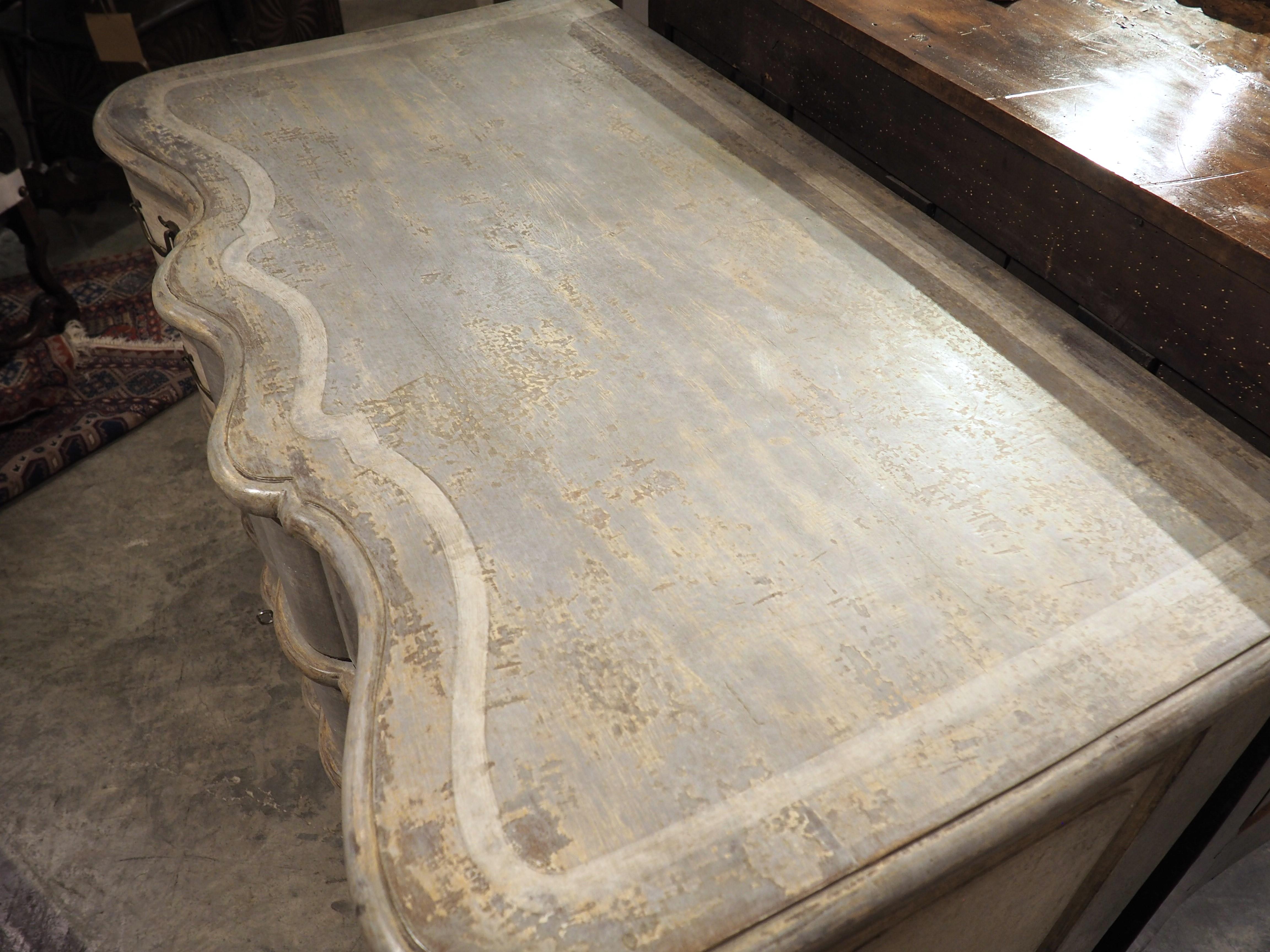 Esta antigua cómoda pintada de tres cajones tiene un maravilloso frente serpenteante, acentuado por púas angulosas donde se unen las curvas. Cada cajón tiene un bocallave de hoja festoneada flanqueado por un par de tiradores de gota de bronce, con