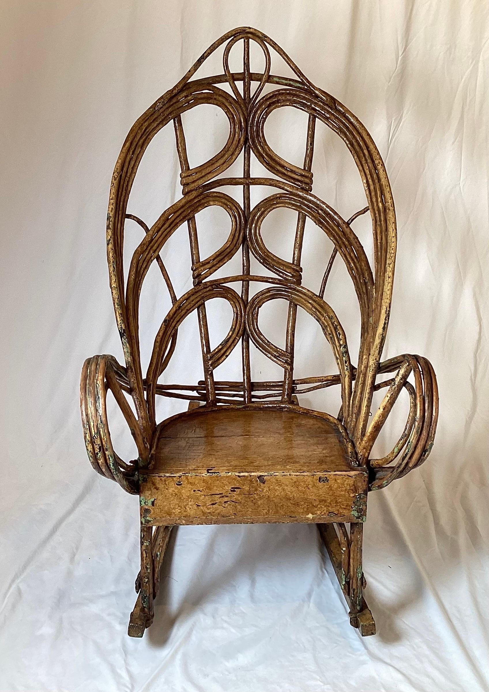 A hand made willow branch Adirondack rocking chair with layers of old paint. The rocker with bands of willow branches shaped to form the back, arms and frame with flat wood panels for the seat. The overall color is amber with hints of earlier green