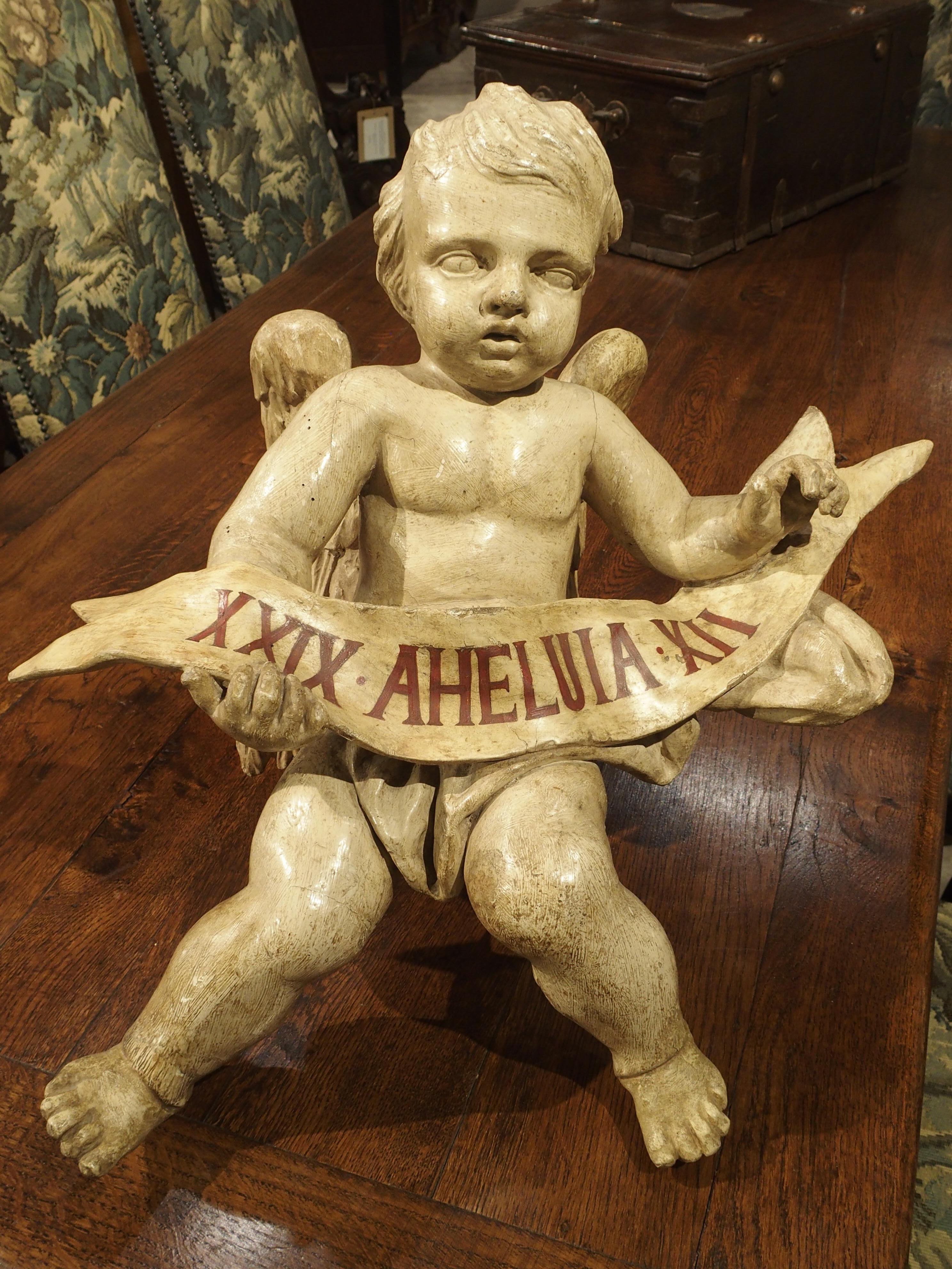 This is a carved and painted wooden cherub statue from Italy. On the back, between the cherubs wings, is an eyelet for hanging. It was originally commissioned by and hung in a private chapel or church. It has been expertly carved as evidenced by