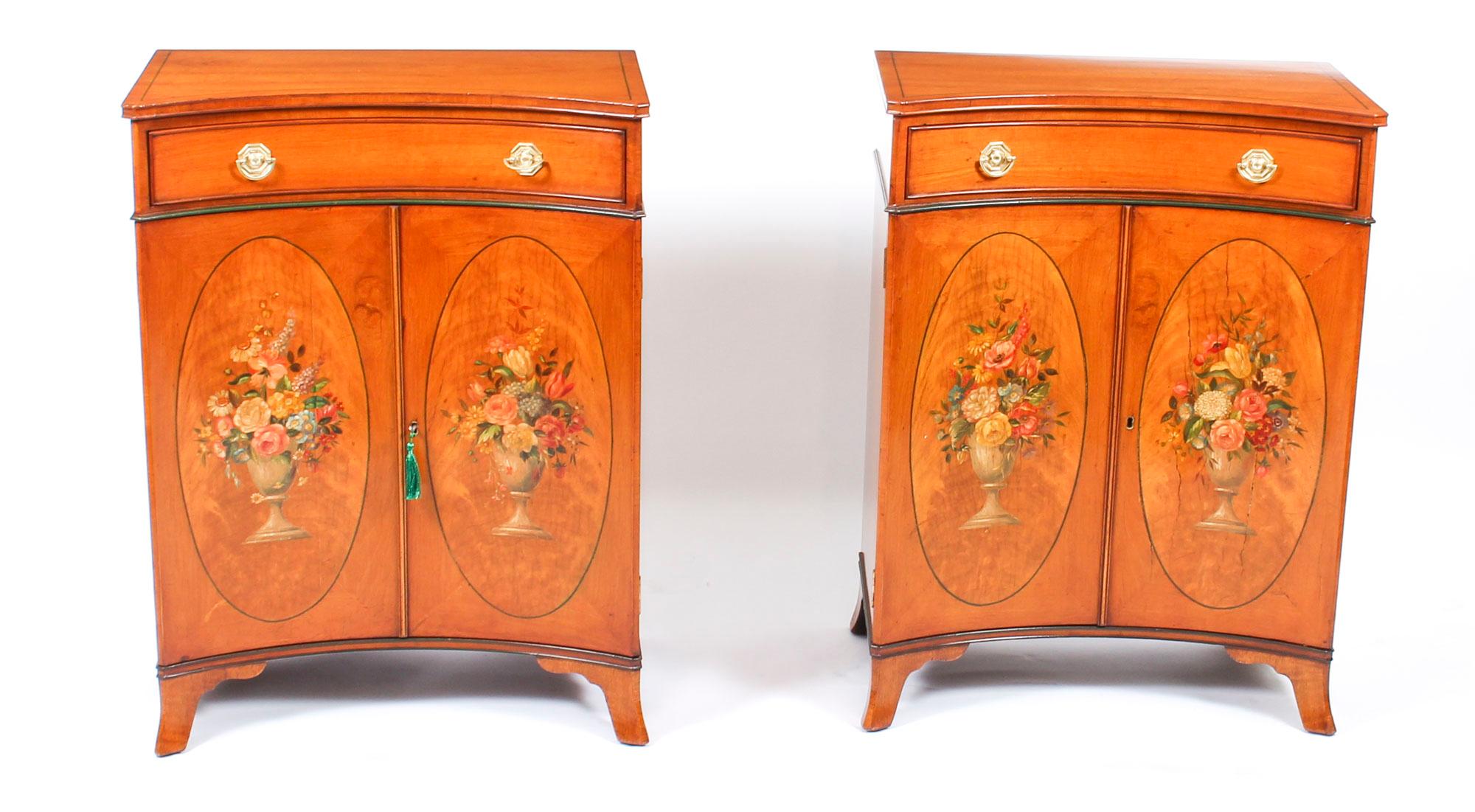 This is a gorgeous pair of antique Adam Revival satinwood concave side cabinets with beautiful hand painted floral decoration, dating from the late 19th century.

Each cabinet has a useful frieze drawer above a pair of cupboard doors, with oval