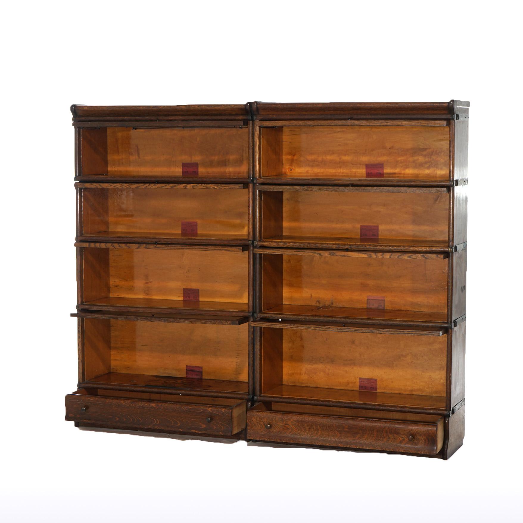 An antique pair of Arts and Crafts barrister bookcases by Globe Wernicke offer quarter sawn oak construction with four stacks, each having pull-out glass doors with single leaded glass door, raised on an ogee base with maker label as photographed,