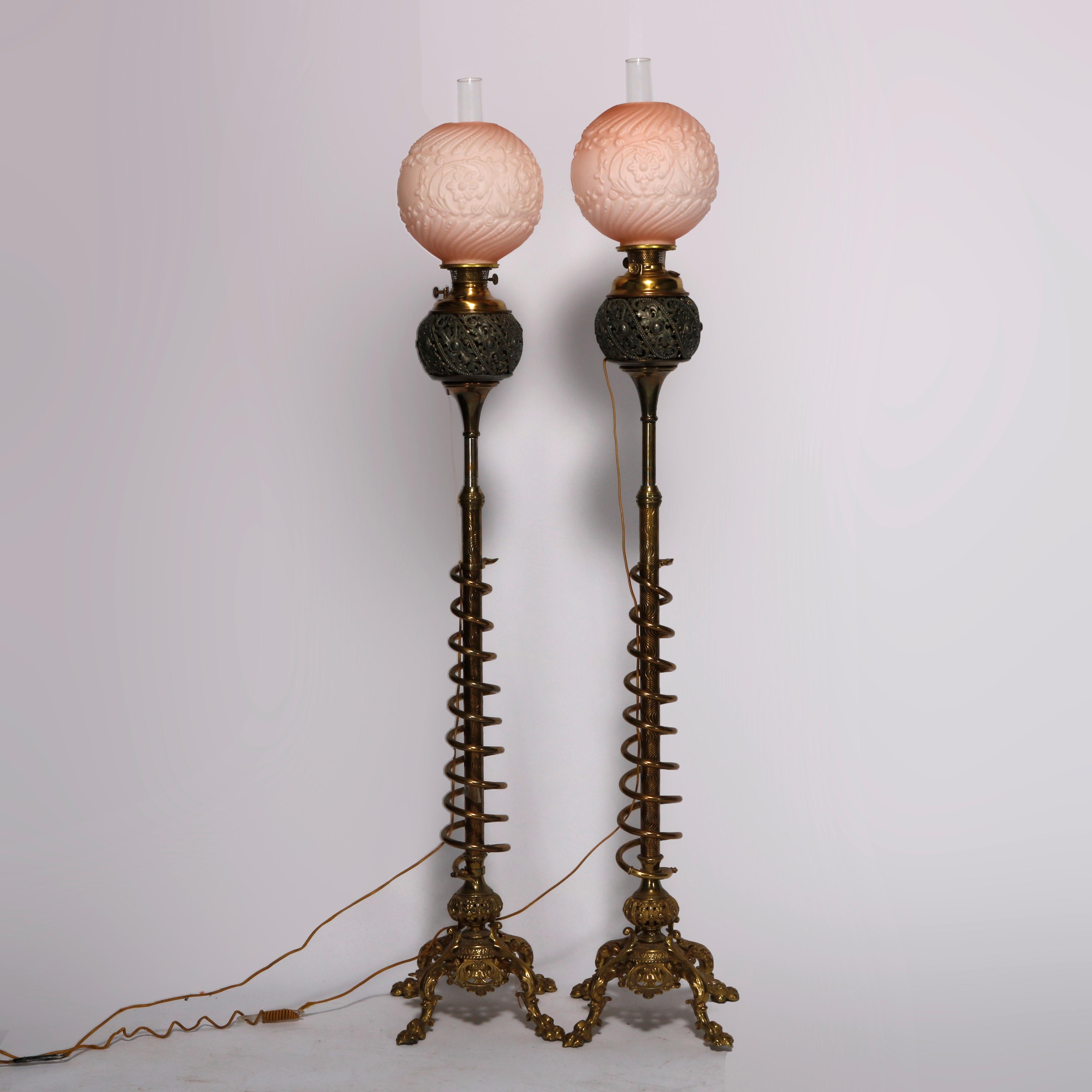 An antique pair of matching piano lamps by Bradley and Hubbard offers foliate embossed glass shade over brass and white metal construction with pierced foliate font over extending column having spiral casing, raised on cast foliate footed base,