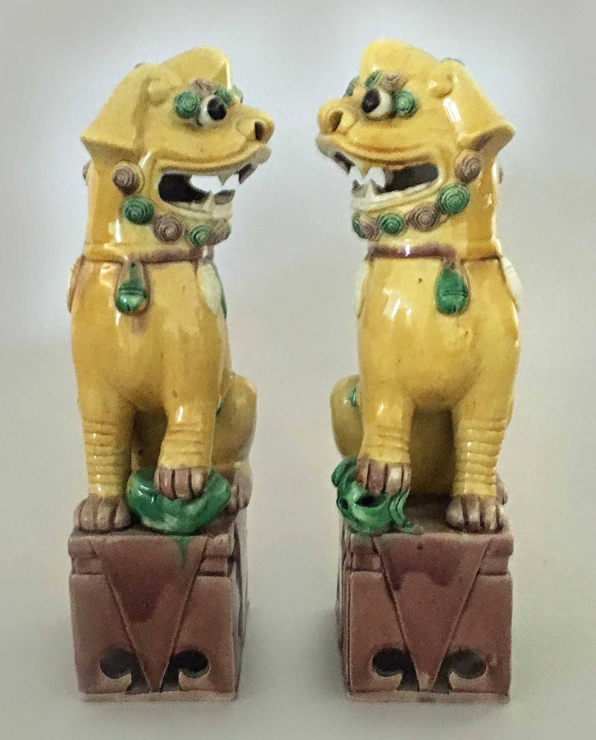 Pair of Chinese foo dogs, the animals is decorated in yellow and green and mounted on pierced brown bases. The female is holding her baby underfoot and the male has an orb underfoot.