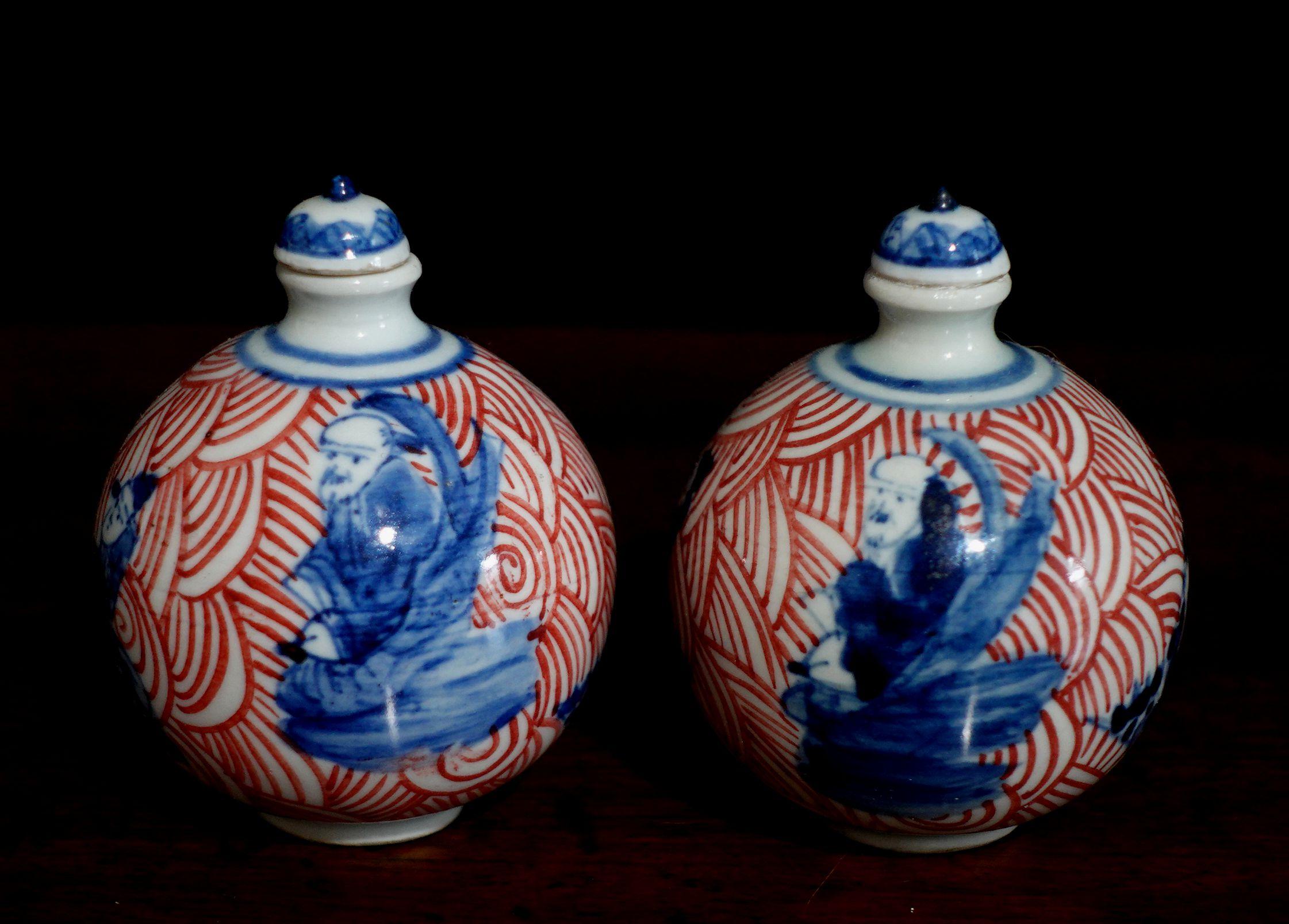 Two Chinese porcelain snuff bottles decorated with Imari blue and red hues and sitting figures, marked along the underside. CIRCA: 19th Century.
 
