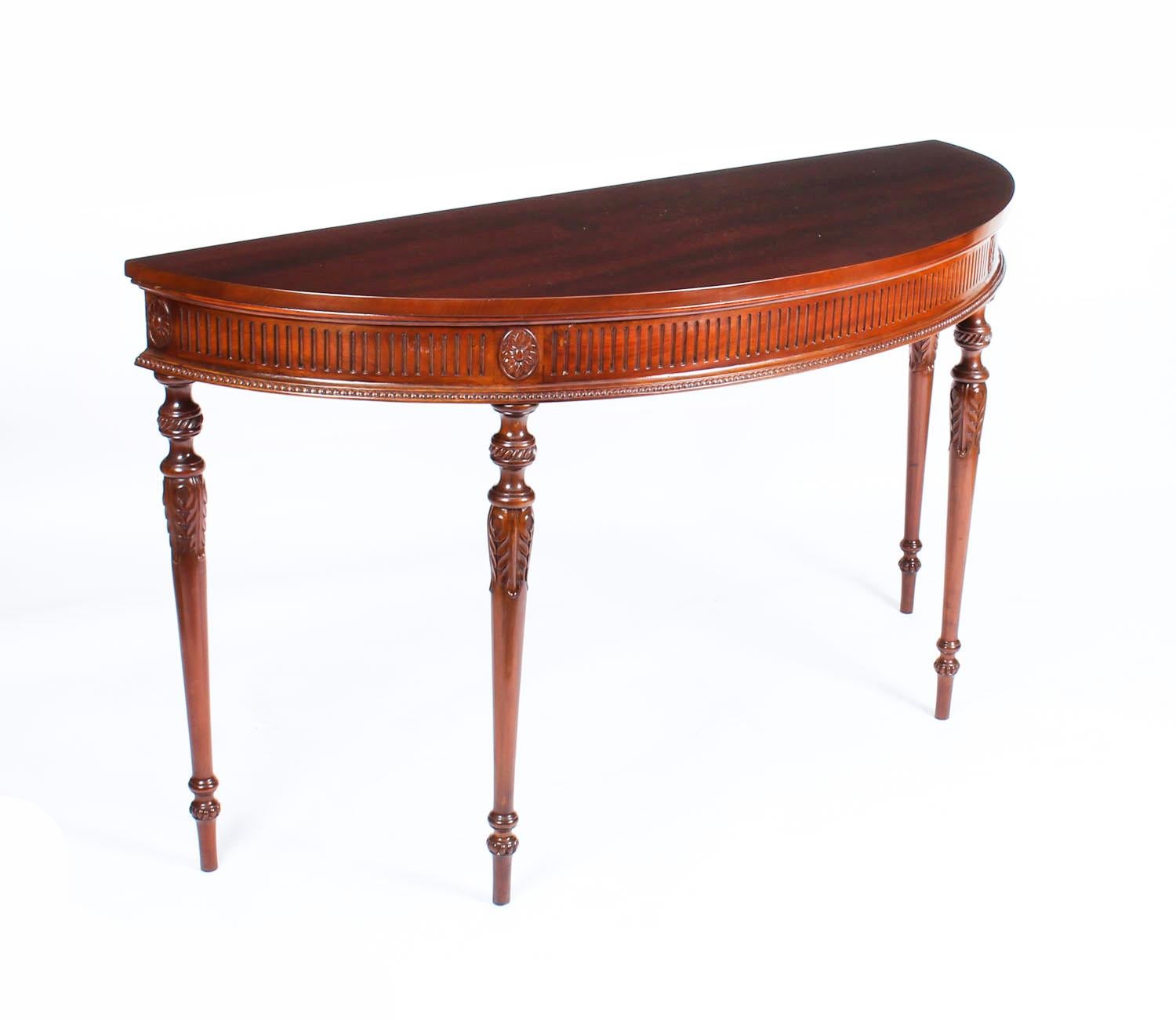 This is a lovely antique pair of English Edwardian mahogany demilune console tables in, dating from circa 1900.

The half-round console table tops feature shallow profiles, the fluted friezes beautifully marked with flower heads above bead