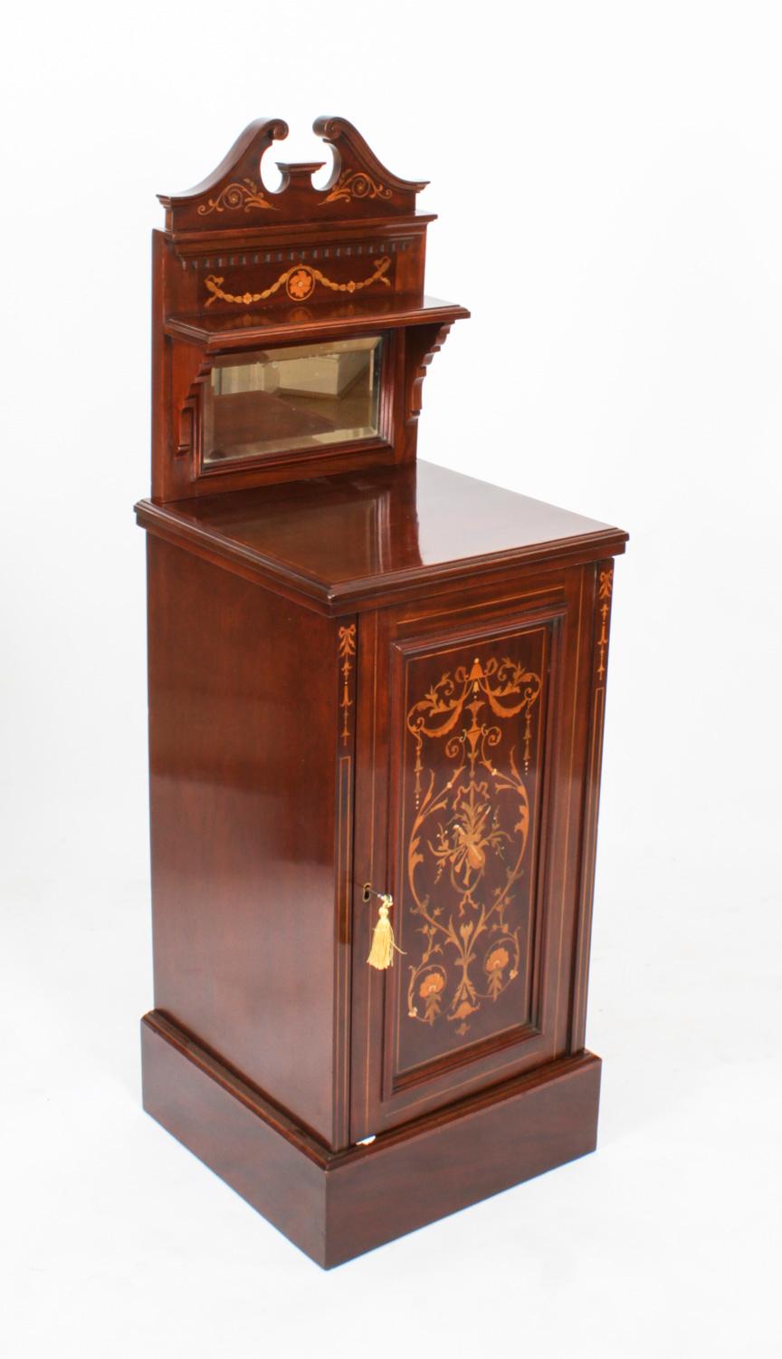 A Pair of Edwardian mahogany and Marquetry Inlaid Sheraton-Revival Bedside Cabinets, the swan-neck pediments above a small shelf with bevelled glass plate below, the moulded top above a hinged cupboard door, one enclosing two sliding trays, the