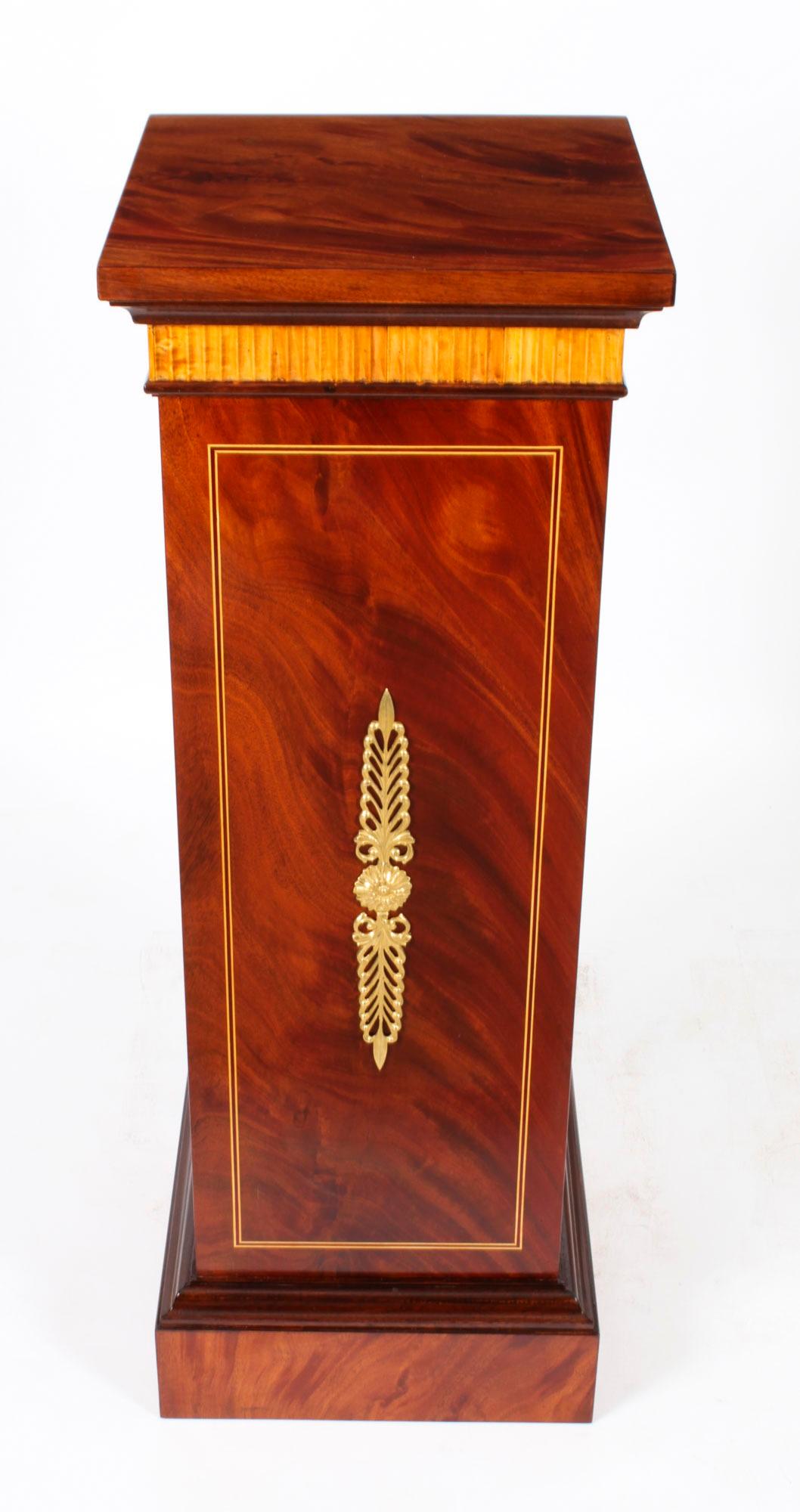 This is a gorgeous pair of antique Empire Revival ormolu mounted flame mahogany  pedestals, circa 1930 in date.

Each with a square stepped top above a gilt reeded frieze on a rectangular column decorated with satin wood crossbanding and omolu