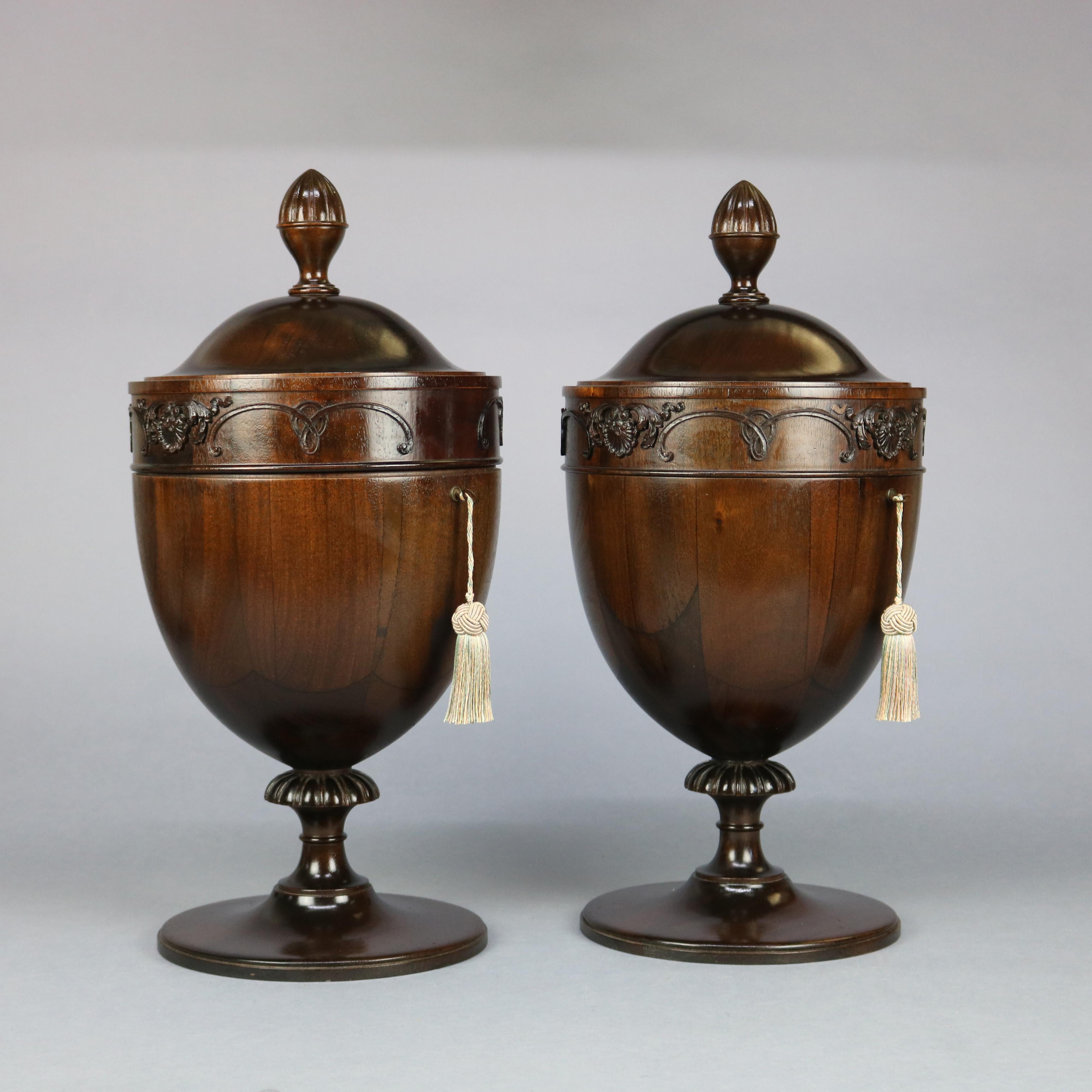 A pair of antique English Georgian III knife boxes offer mahogany construction in urn form with telescoping lid having carved finial and foliate carved band opening to compartmentalized interior, vessel raised on gadroon plinth seated on tall