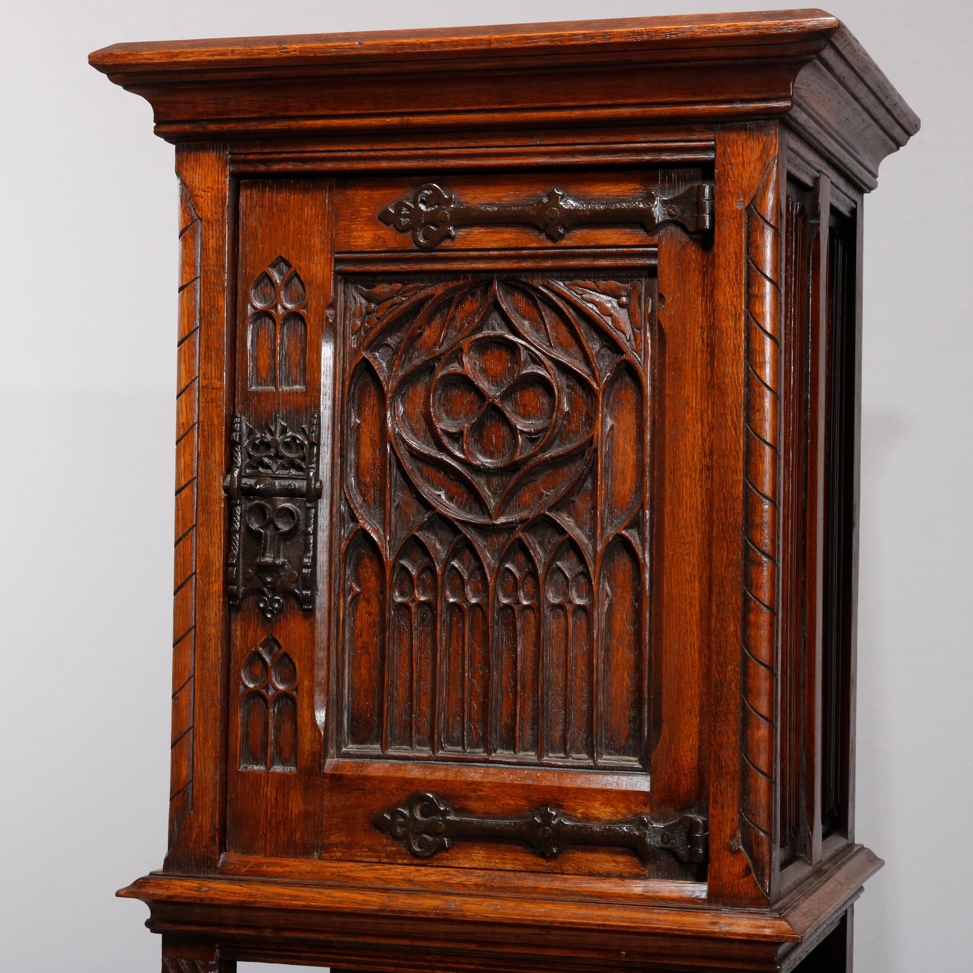 An antique pair of English Gothic Revival side cabinets offer oak construction with upper cabinet having carved door having ornately cast iron hardware and strap hinges surmounting lower display, circa 1890.

Measures- 50