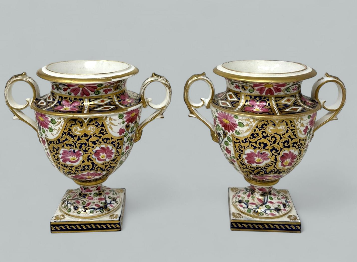 Un par excepcionalmente fino y bastante raro de jarrones de dos asas Royal Crown Derby pintados a mano de contorno campana, principios del siglo XIX, época de la Regencia. 

Con dos asas de volutas doradas sobre una máscara de cabeza de león y
