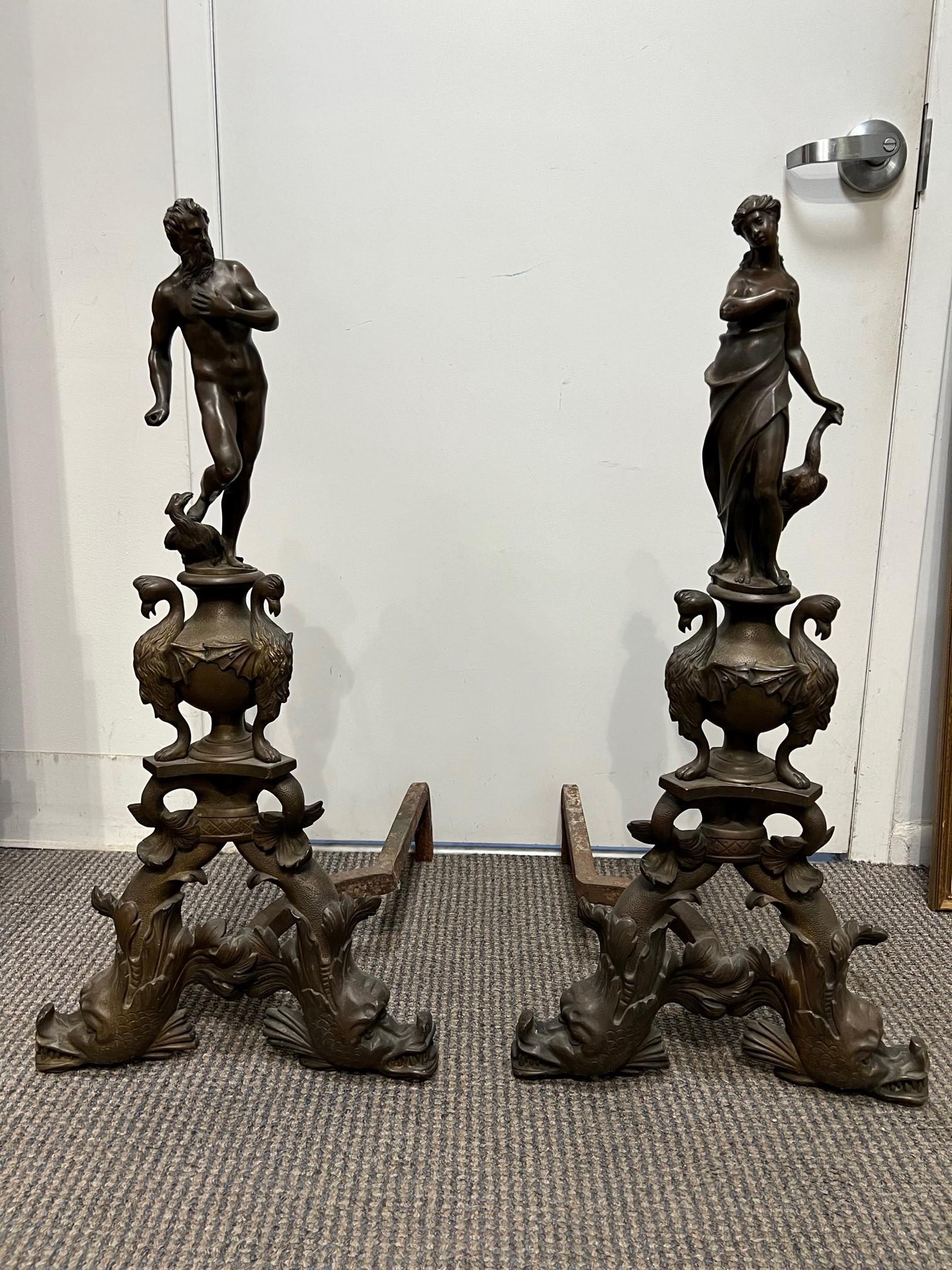 Antique pair of figural bronze andirons of a Man and Woman from Paris France. This is an impressive pair of andirons with dolphin fish as the base holding a urn with three winged griffons, birds maybe Phoenix. On top of the urn stands a man and
