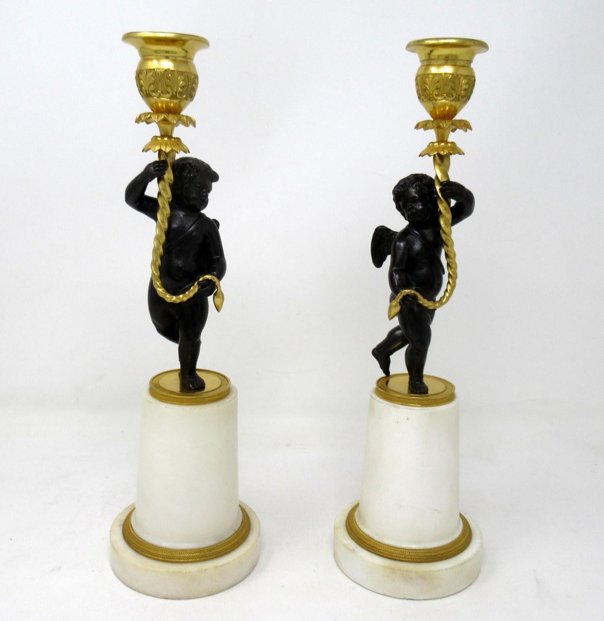 An exceptional pair of French single light creamy off-white statutory marble and bronze mantle candlesticks of medium proportions, first half of the 19th century, possibly regency period.

Each bronze winged scantily clad cherub or putti holding a