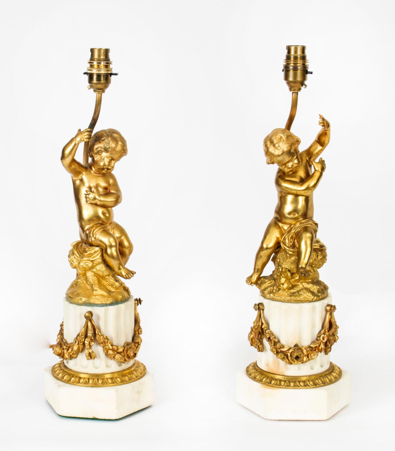 A magnificent antique pair of French ormolu table lamps with shades, Circa 1920 in date. 

The stems formed as putto seated upon naturalistically modelled stumps, each upon a fluted marble column base detailed with ormolu floral swag, and a