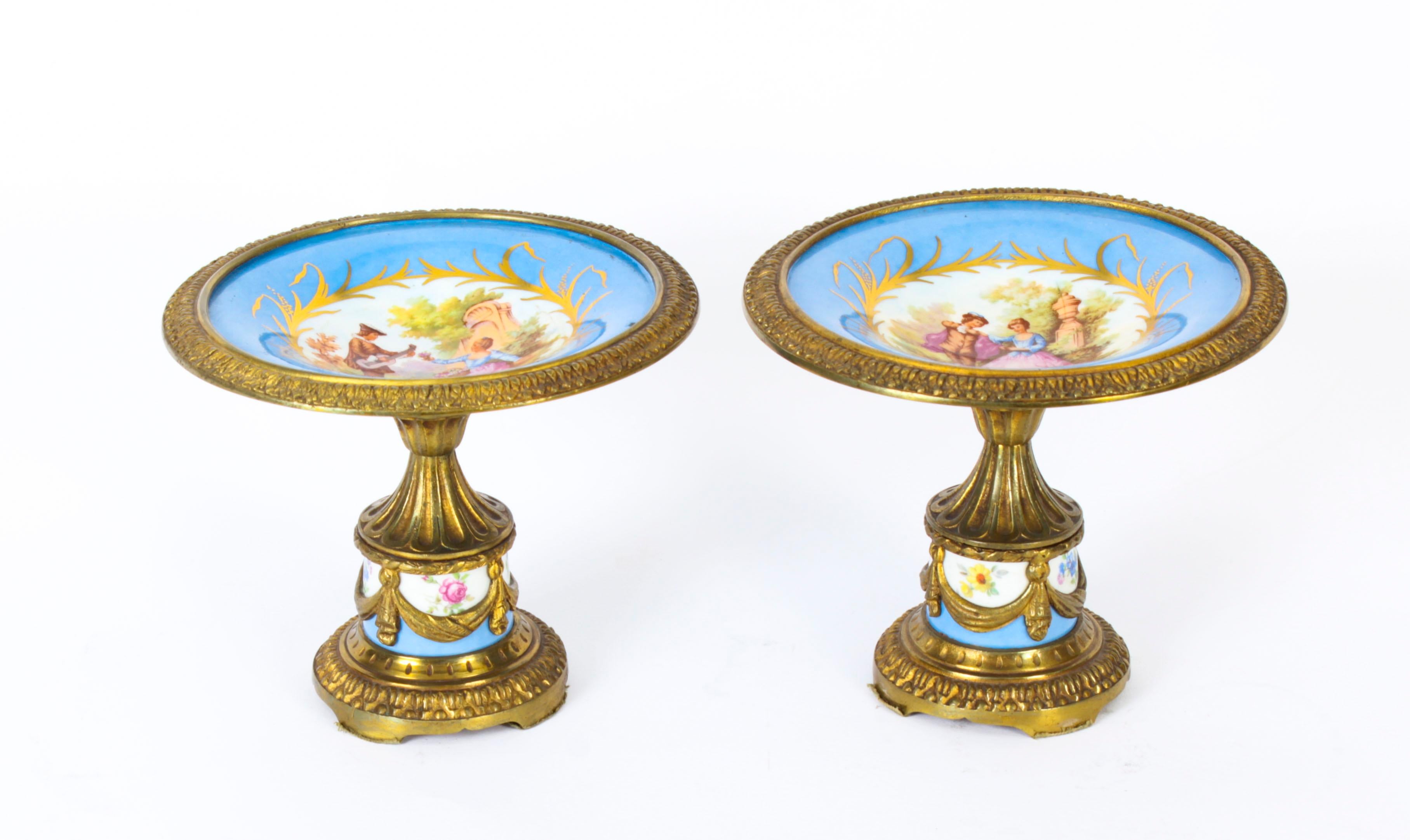 This is a beautiful antique pair of French ormolu mounted Sevres porcelain tazzas, in the Louis XV manner, Circa 1870 in date.
 
The tazzas with a bleu celeste ground are superbly decorated with circular painted panels depicting romantic courting