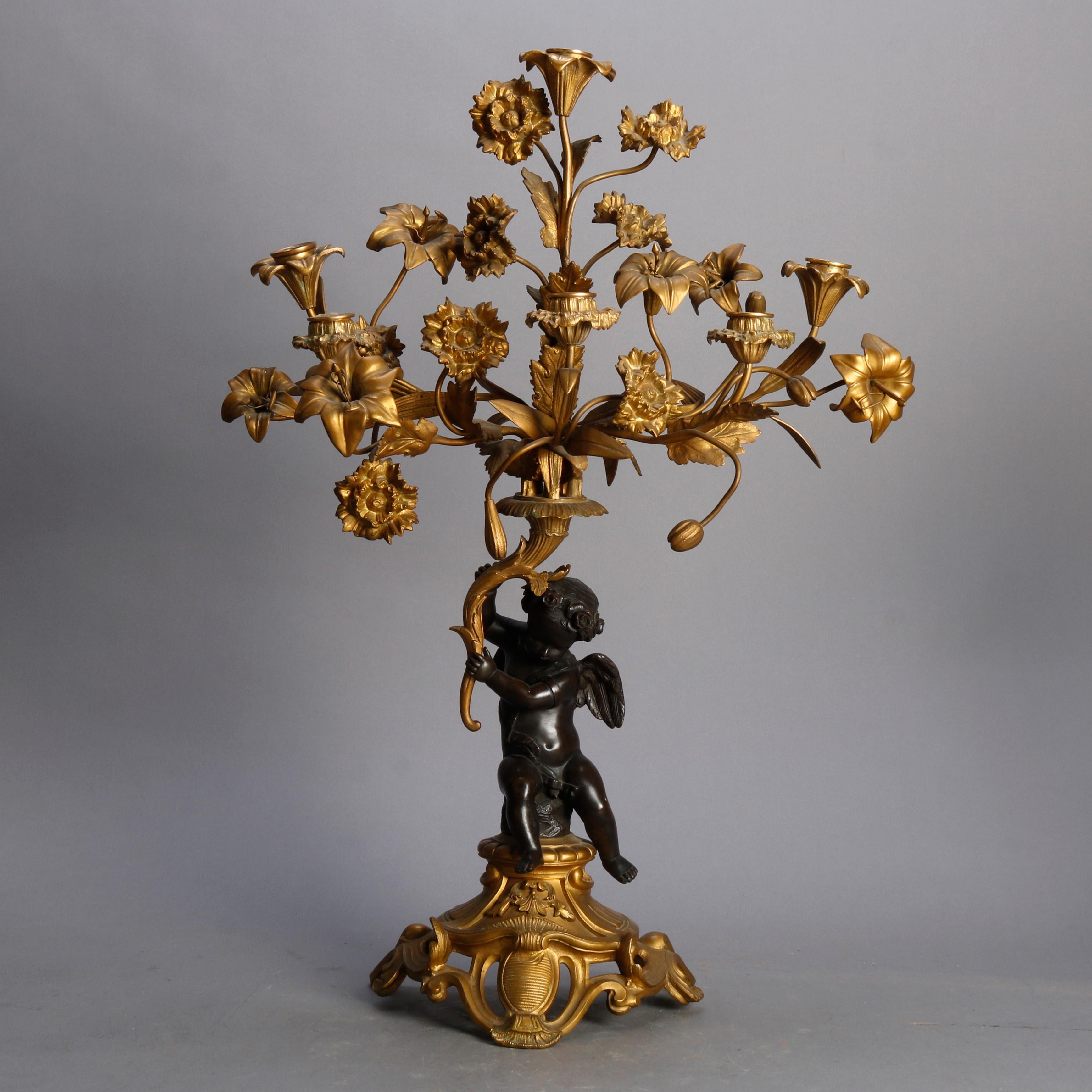 An antique pair of French Rococo figural parcel-gilt candelabra offer gilt metal foliate and floral form arms terminating in candle sockets surmounting Classical cherub form columns and raised gilt pierced scroll and foliate from bases, 19th