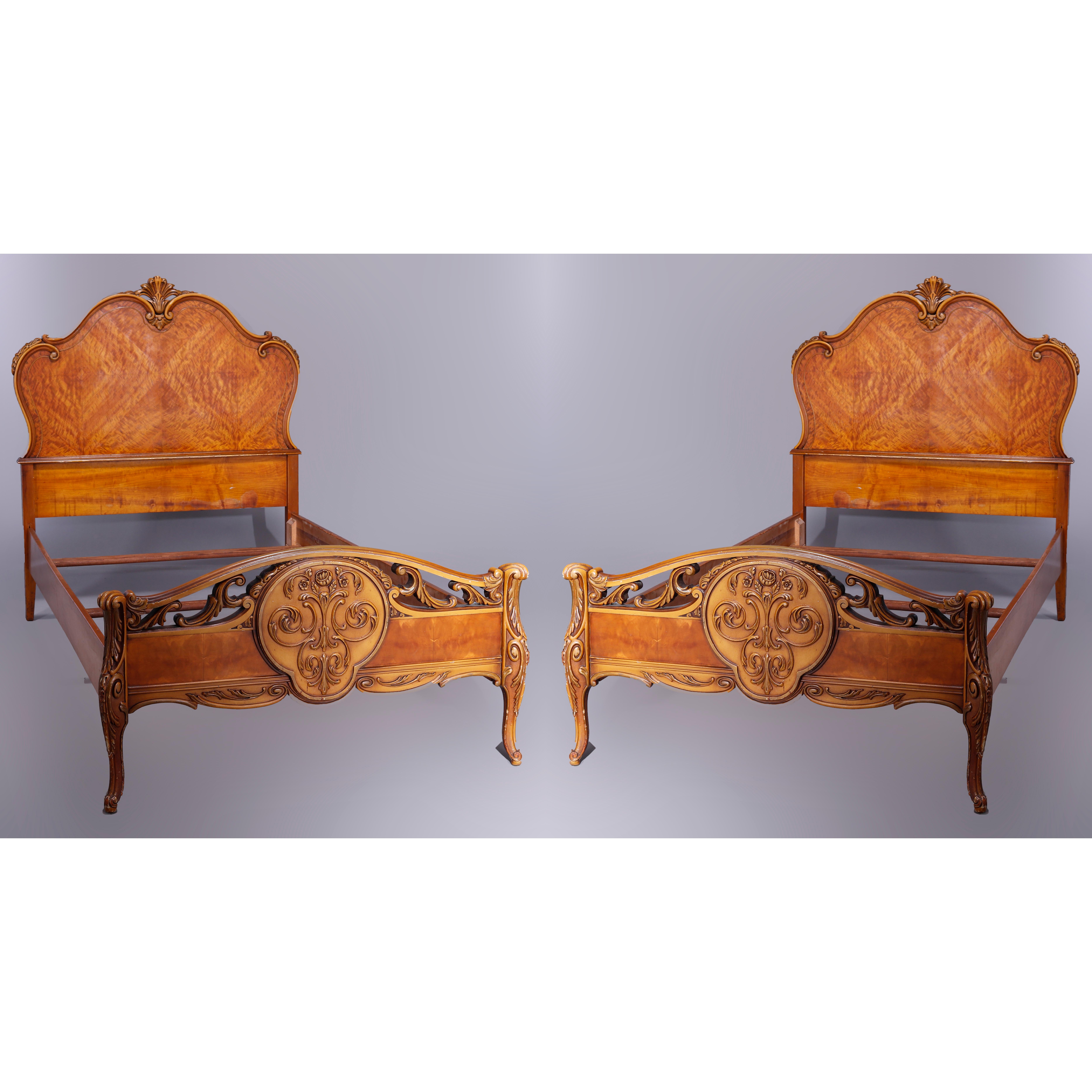 An antique pair of French style twin bed frames offer shaped head and foot boars with bookmatched satinwood facing, carved and pierced foliate elements, carved medallion of footboard having scrolled foliate elements, raised on cabriole legs