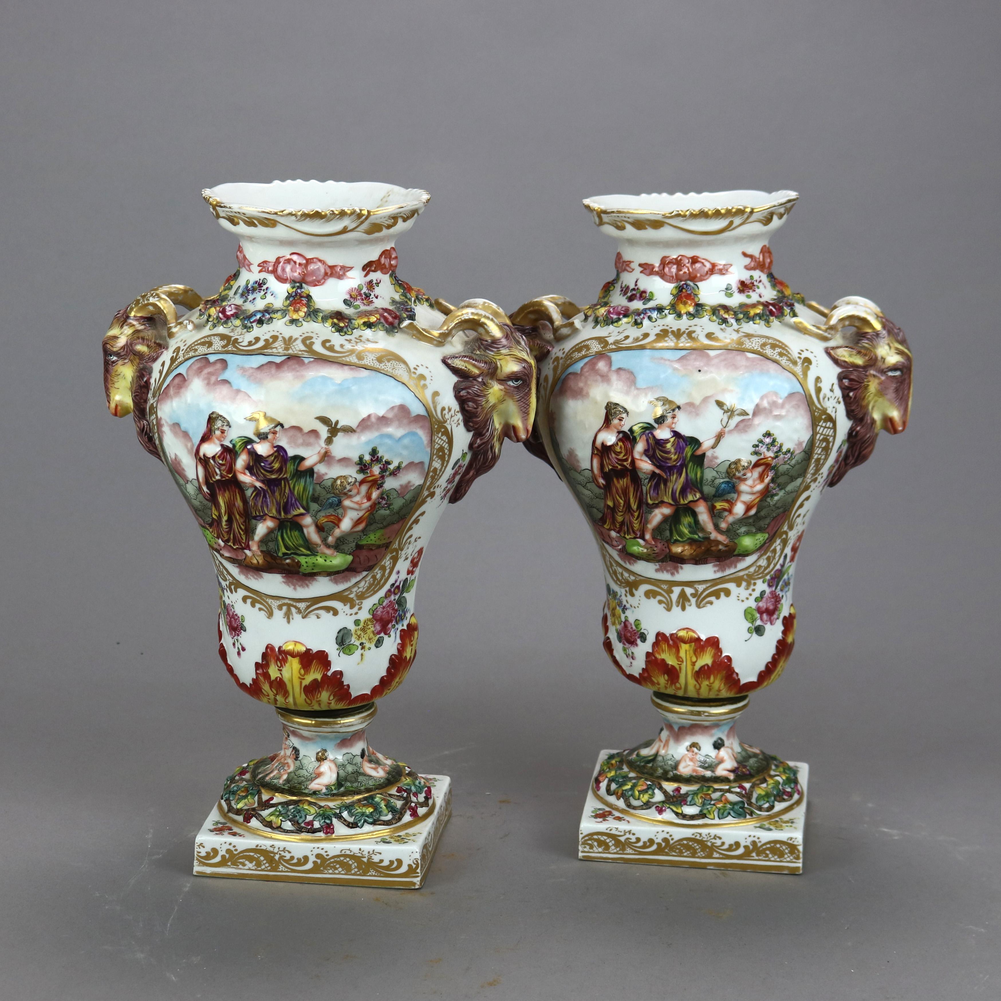 An antique pair of German urns by Potschappel of Saxony offer porcelain construction with central hand painted Classical genre scenes in relief and double figural goat handles, gilt highlights throughout, five prong crown N mark as photographed,