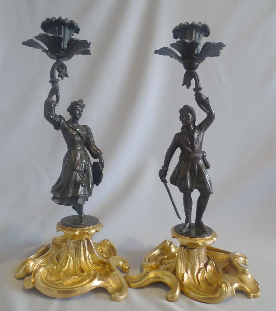 Antique Greek Revolution or Helenistic pair of figural candlesticks of a patinated bronze Greek Revolutionary hero and a Greek woman. The figures standing on a gilt bronze rococco base. The Hero with sword in hand and dagger in belt with embroidered