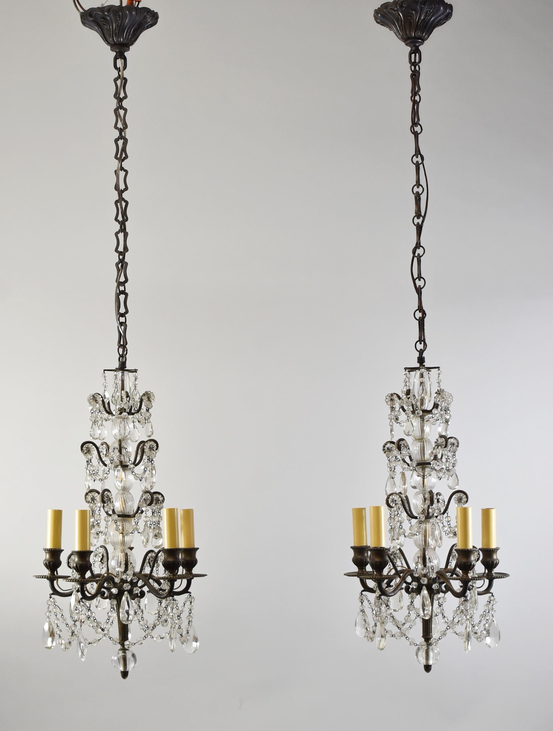 Pair antique four tier crystal, blown glass and brass chandeliers. Crystal draped beads with cut floral details. Five candelabra sockets. Center blown and turned glass center stem. Very nice condition. Body measures 19