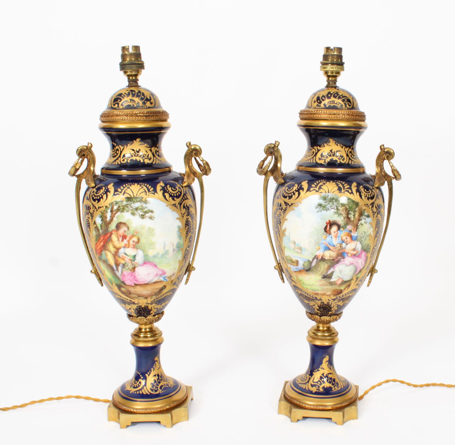 This is an exquisite large pair of French cobalt blue porcelain and ormolu mounted twin handled vases, in the Sevres manner, that have been skillfully converted to electricity, circa 1900 in date. 

The vases are superbly decorated with hand painted