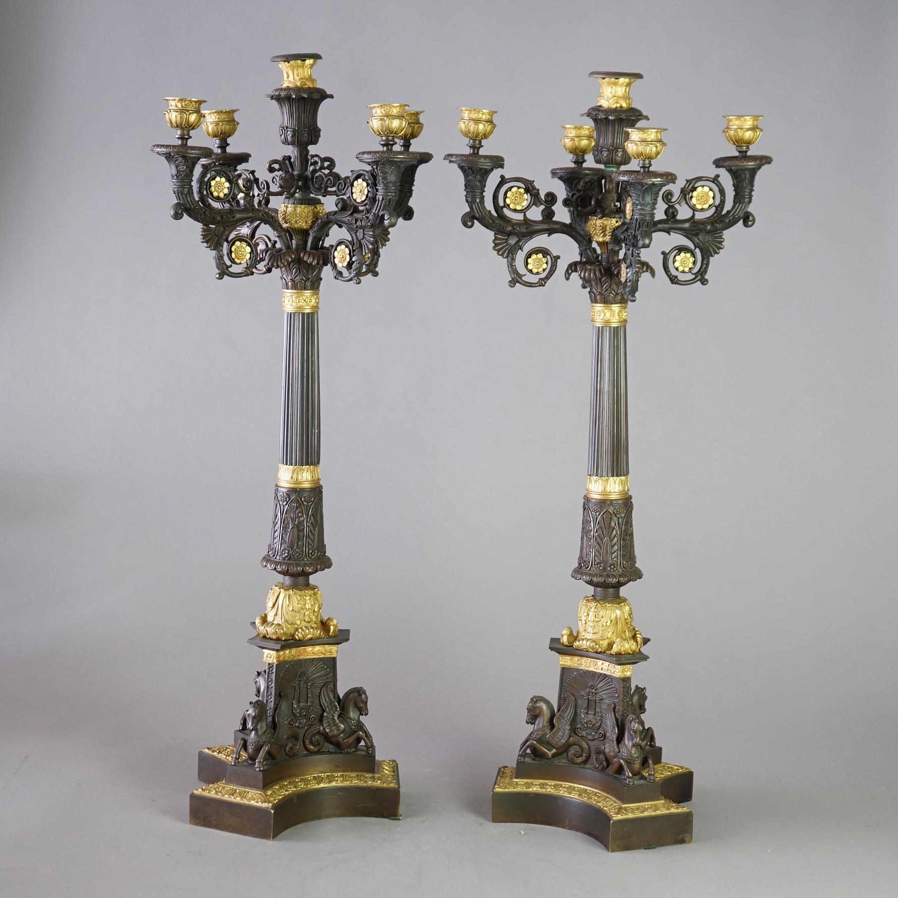 An antique pair of oversized French Empire figural candelabra offer cast bronze construction with scroll form arms with gilt rosettes and terminating in gilt candle sockets over flared and fluted column, raised on Pegasus base; gilt elements