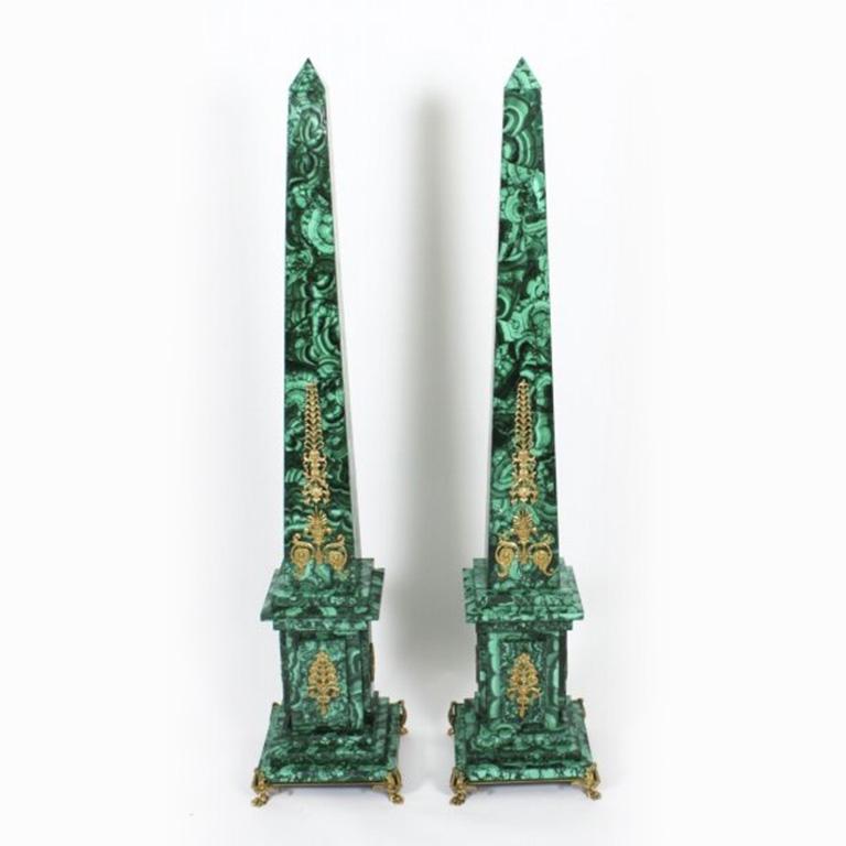 Une paire monumentale d'obélisques néoclassiques en malachite montés en bronze doré sur des piédestaux en acajou, datant d'environ 1920.
 
Les colonnes carrées en malachite se rétrécissent en forme de pyramide et sont ornées de montures