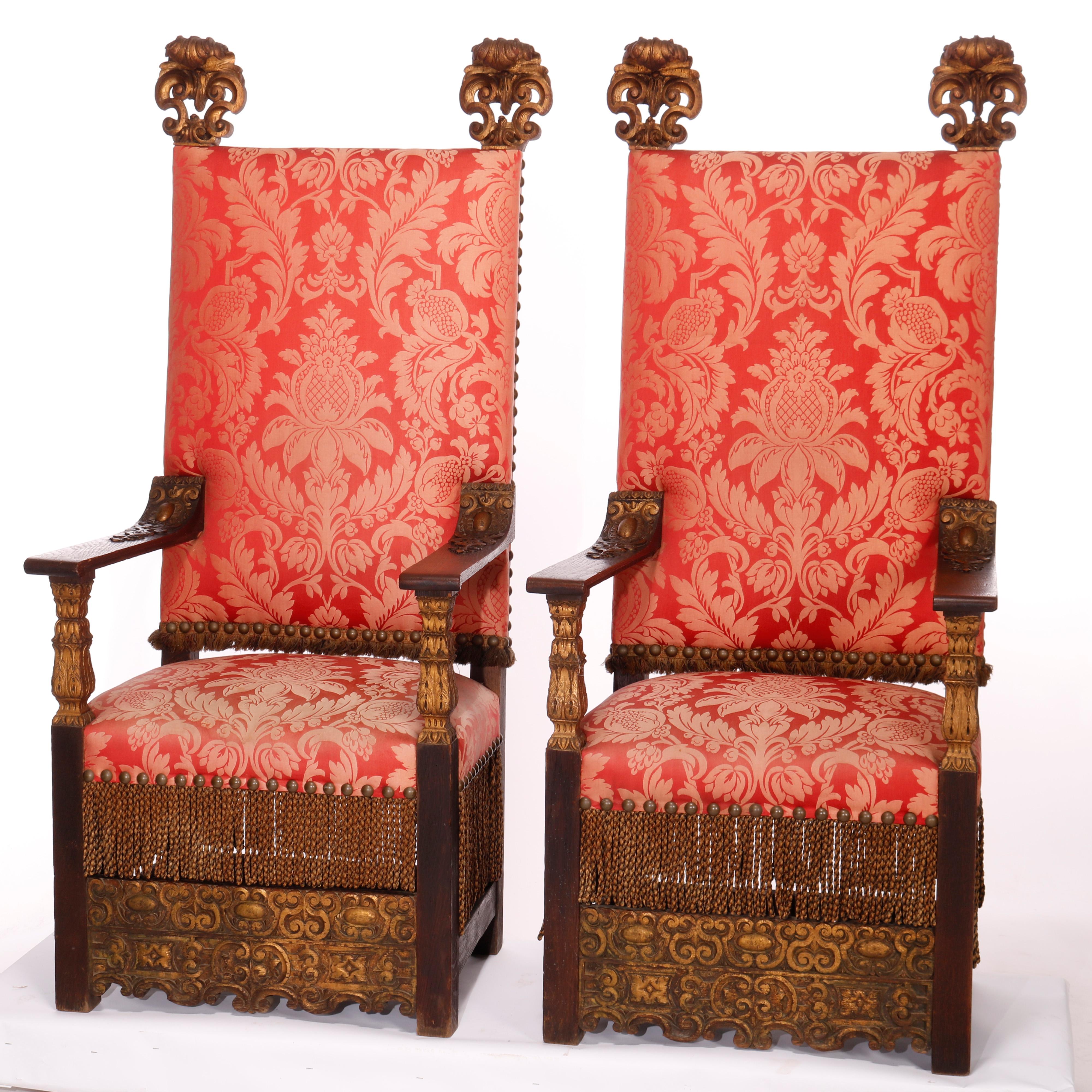 An antique pair of large tall-back Moorish style throne chairs offer oak construction with upholstered backs having carved giltwood acanthus elements, oversized upholstered seats with fringe and carved stretchers, foliate decoration throughout,