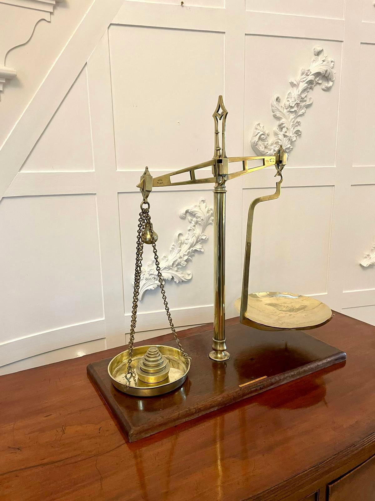 Pair of antique brass scales standing on a mahogany base. A brass centre column having a shaped arm to the left holding a removable brass bowl.  The second bowl to the right is held by a brass chain and holds the original set of brass weights.