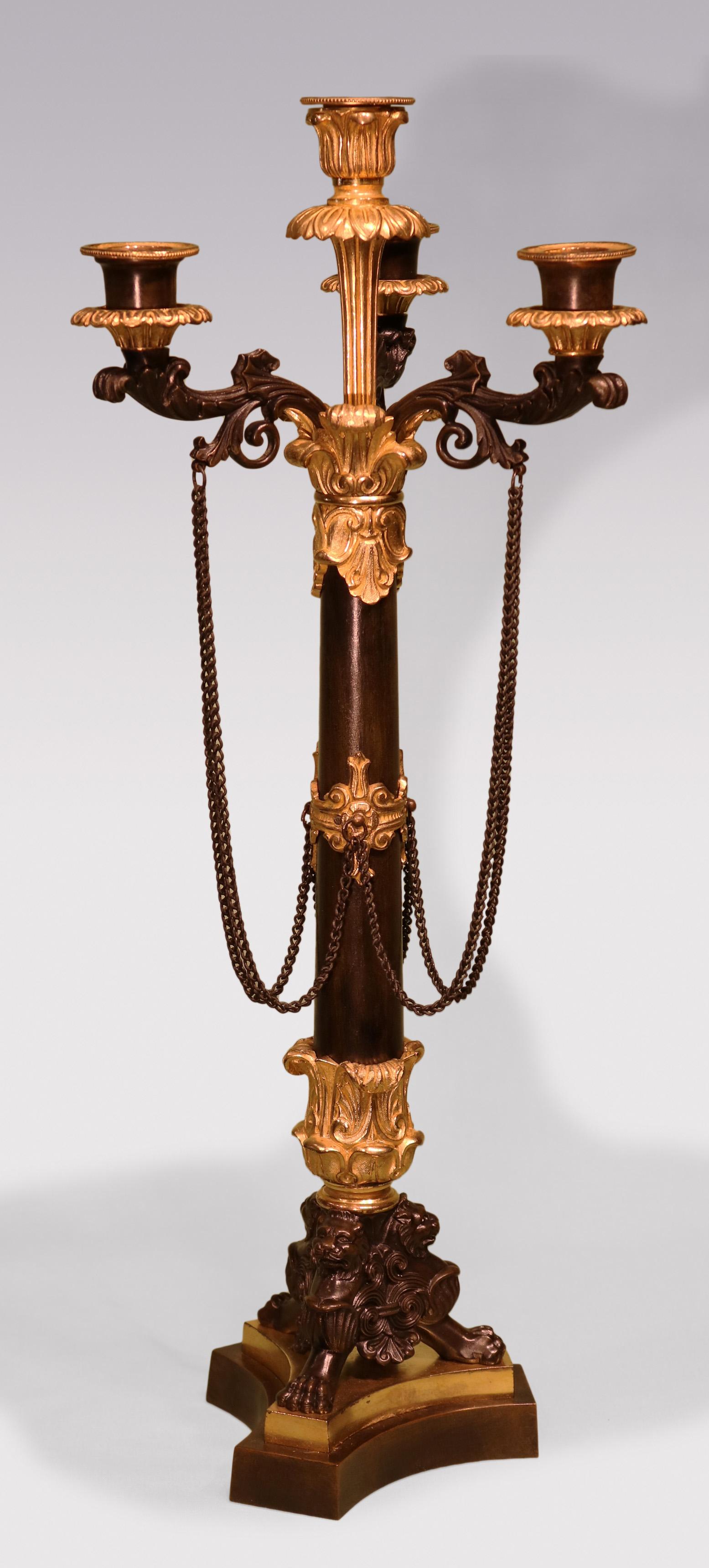 Coppia di candelabri a 4 luci in bronzo e ormolu della metà del XIX secolo, con bracci a voluta con decorazione a catena sopra steli affusolati con montature applicate, sollevati su gambe triformi a testa di leone che terminano su basi a plinto a