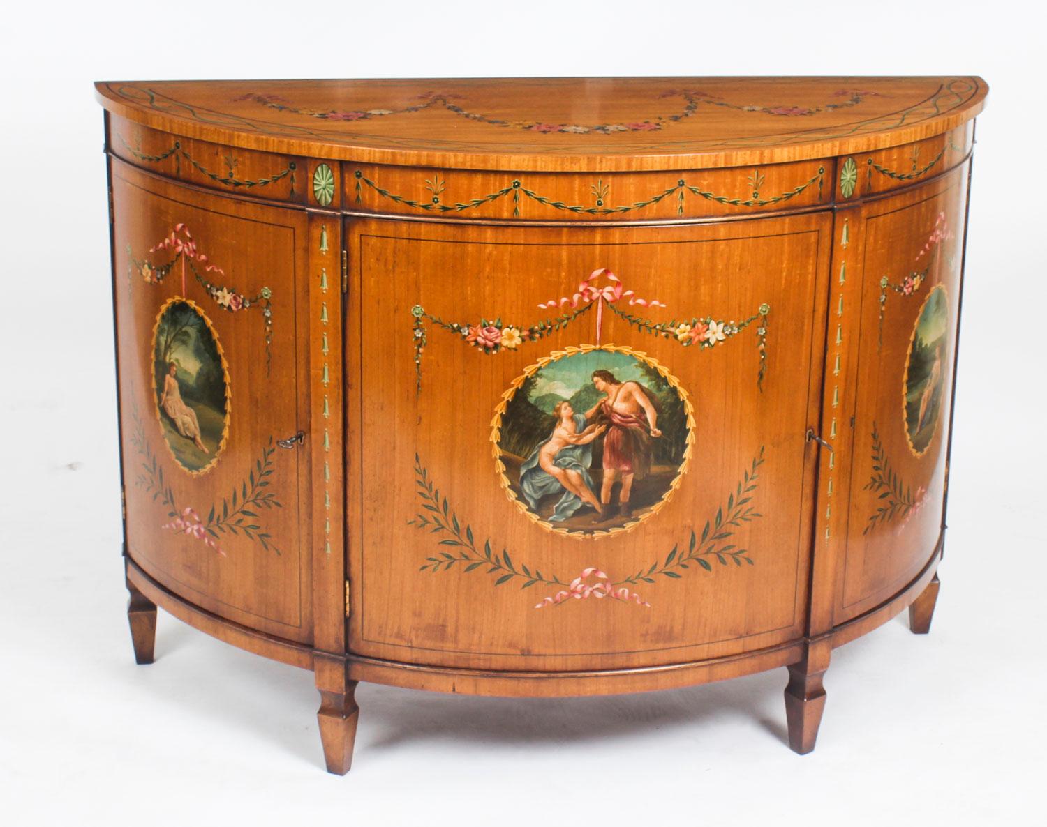 This is a gorgeous pair of antique Adam Revival satinwood demi lune commodes with beautiful hand painted decoration, daing from the late 19th century.

Each commode has striking hand painted decoration of classical scenes, floral garlands and
