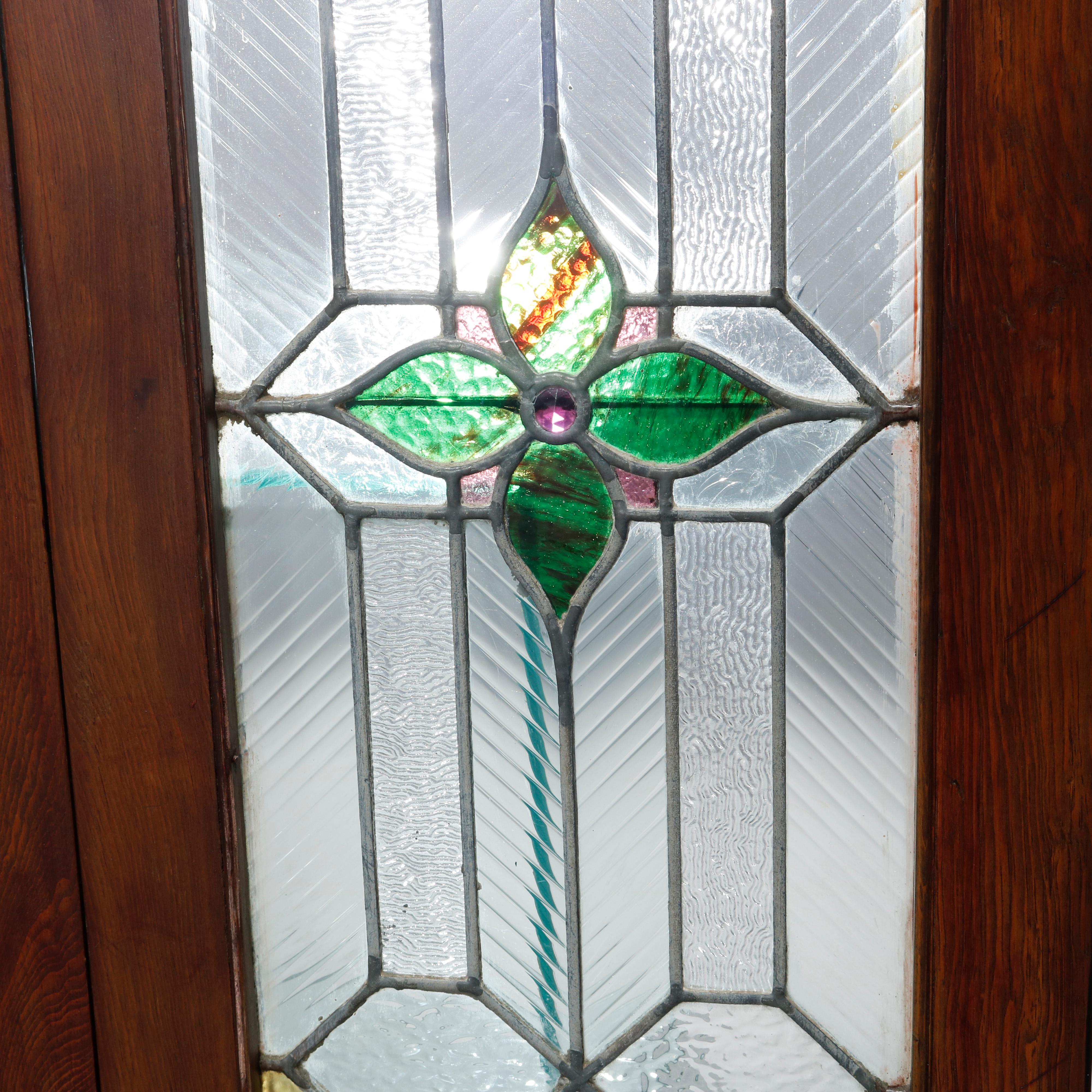 An antique pair of arts and crafts windows offers leaded jeweled and stained glass with central foliate element, seated in wood sash, c1910

Measures: 35.5