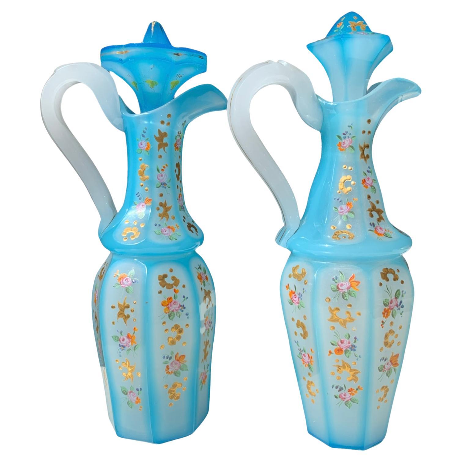 High-quality pair of pitchers with stoppers, made of opal-alabaster overlay glass, cut and decorated all around with colorful gilded enamel work, the white opaque glass is cased with a blue layer of opaque glass, circular body richly enameled with