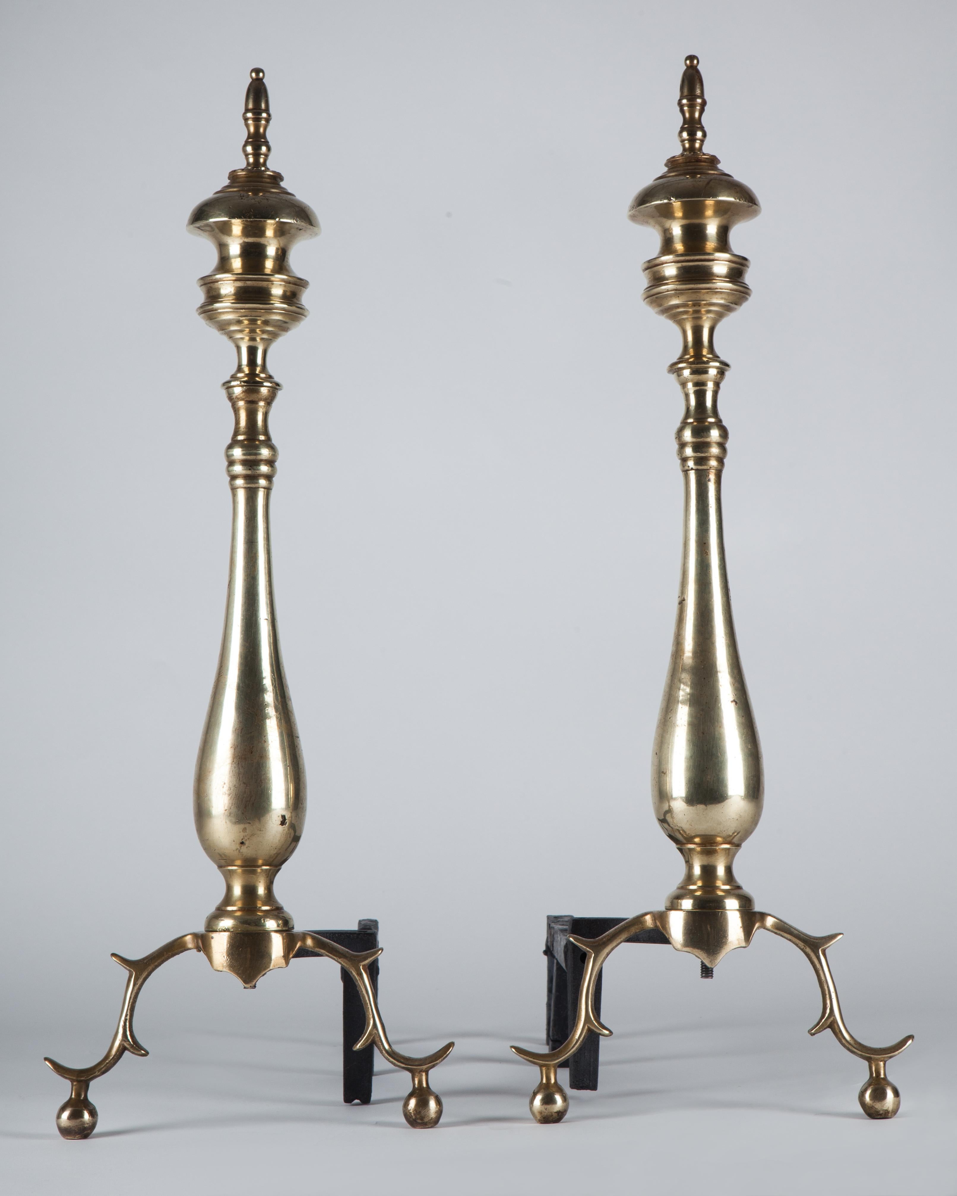 A pair of brass andirons with turned bodies and delicate cast legs terminating in ball feet. In an age-worn brass finish. Circa 1920.

Dimensions:
Overall: 23-1/2