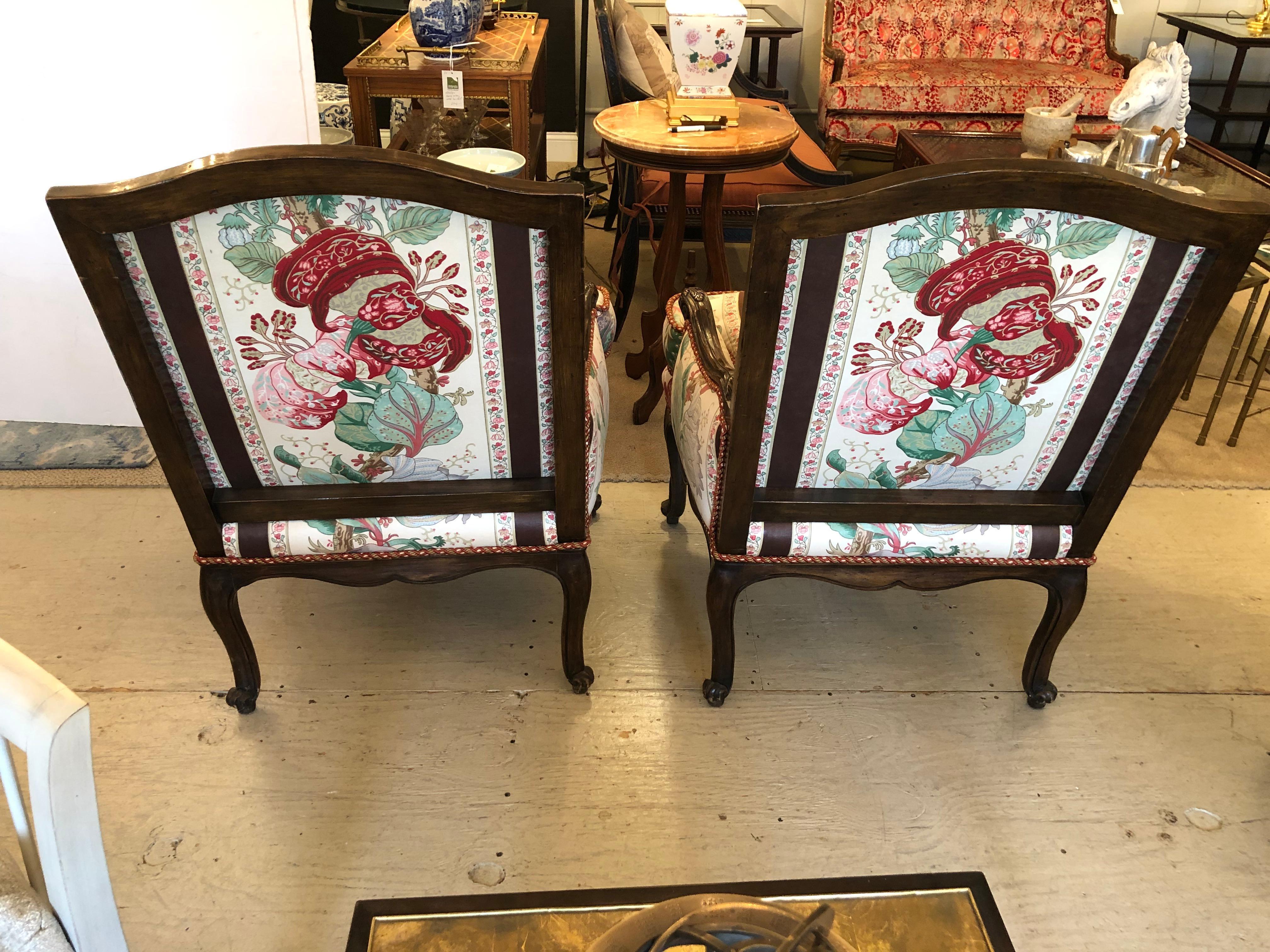 Superb luxurious pair of antique carved walnut and chintz upholstered bergeres that ooze quality. The upholstery on these large club chairs is embellished with coordinating maroon rope trim and the seats are cloud like and down filled. Unbelieveably
