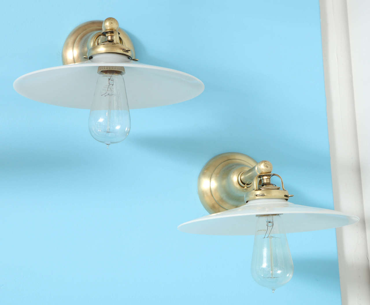 Pair of vintage brass wall lights or sconces with antique white milk glass disk shades. USA, circa 1910. Extended arms hold a 10 inch diameter shade.

Dimensions:
4.5 inch wall plate diameter (part that mounts to wall)
13 inch depth overall or