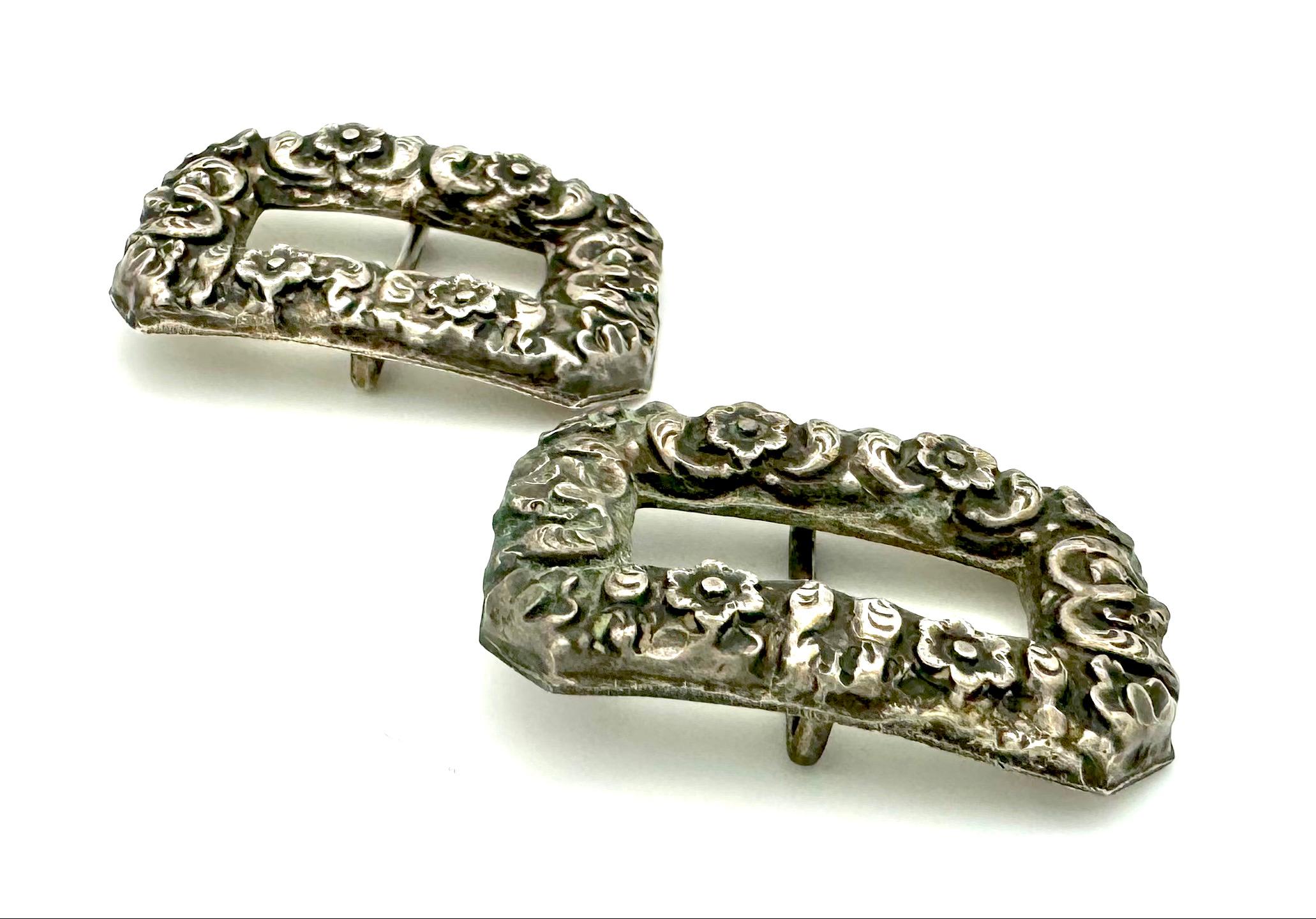 Estos cubrezapatos se crearon en plata en el segundo cuarto del siglo XIX. Las hebillas de zapato de forma octangular están repujadas con un rico diseño de flores y follaje. Normalmente se llevaban en cintas anchas que se cosían al cuero. Las