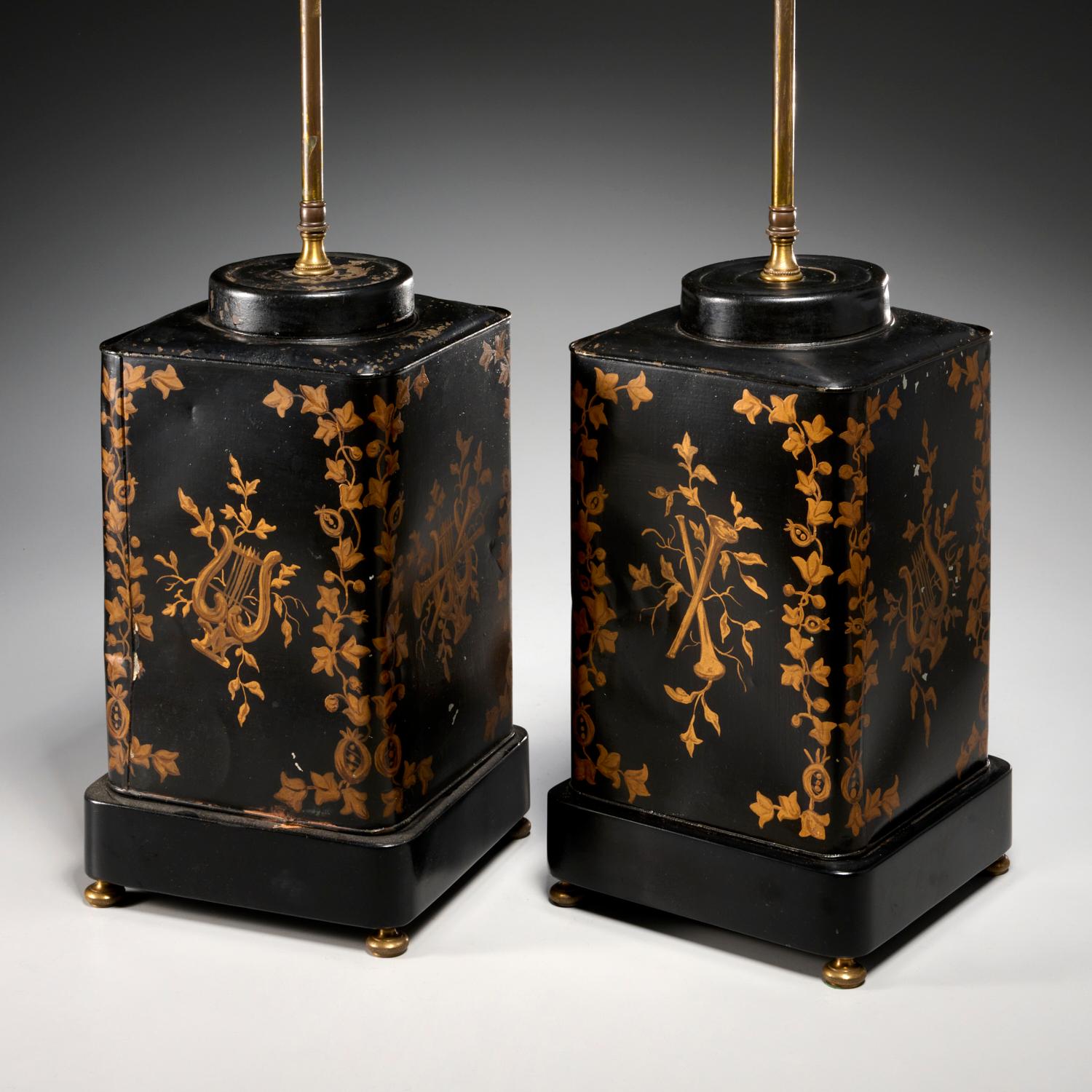 A pair of late 19th c. tea canisters adapted to table lamps each with 3 bulb sockets. With gold painted decorated black enameled metal, each rectangular canister is decorated with bugles and lyres framed by foliate band. Each has an issuing brass