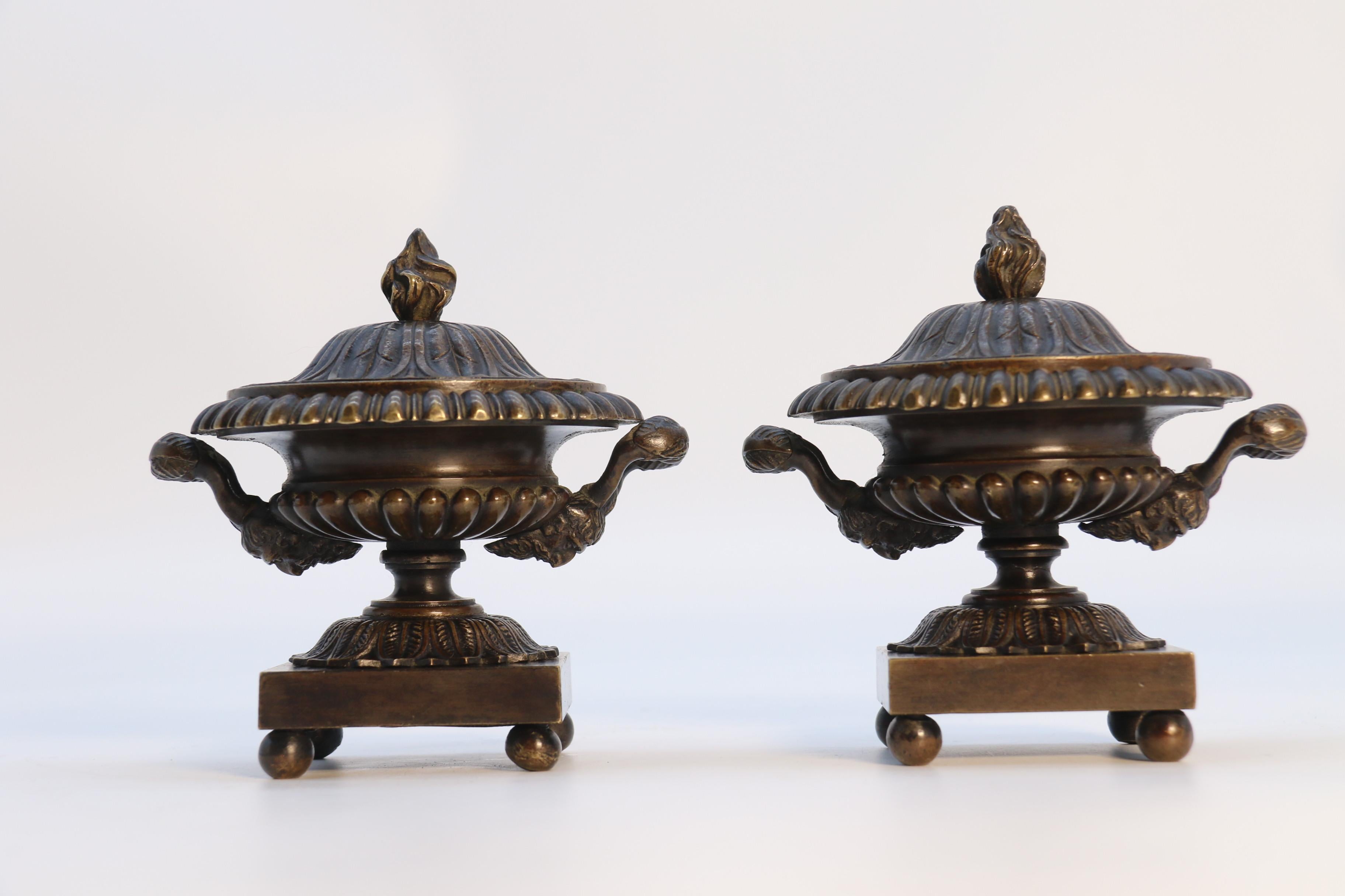 This very elegant pair of English Regency period classical bronze urns are of small proportions and made to a very stylish and sophisticated design. They stand on plain square bases which are raised up onto four small ball shaped feet. The lower
