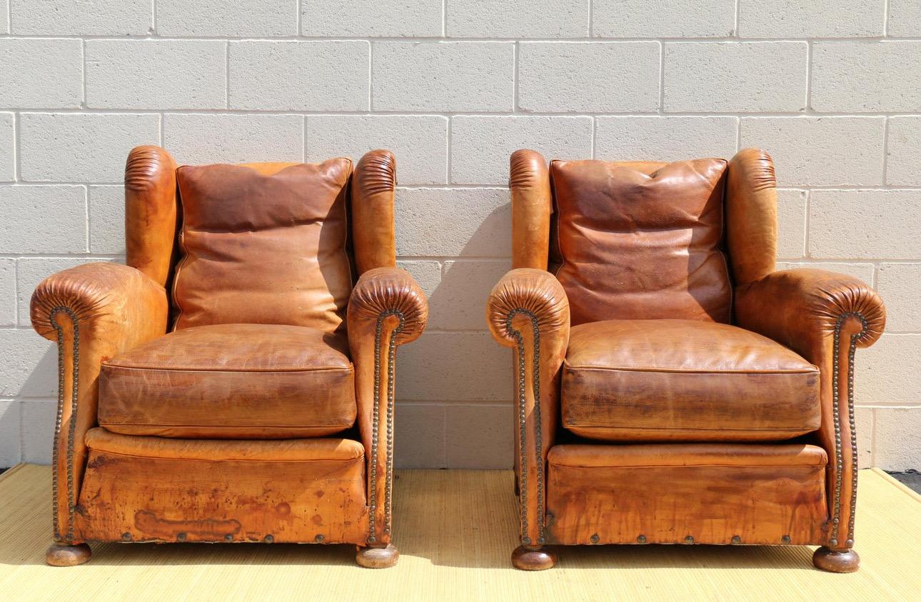 Spectacular pair of French Art Deco distressed lounge chairs made of distressed brown leather, with a wingback. The chairs are in good vintage condition. Both of them have new seat cushions, but the back cushions are still the original ones. You can