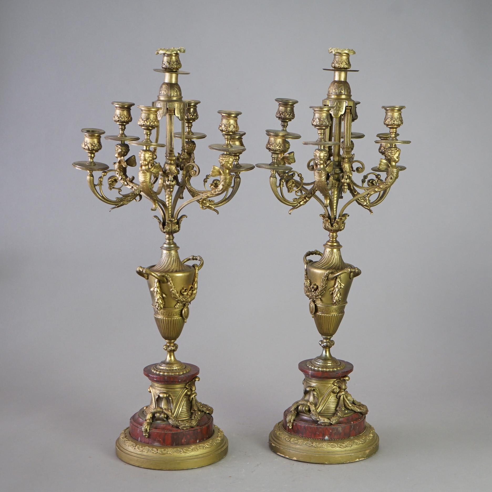 A pair of antique candelabra offer cast and gilt bronze frames with scrolled foliate form arms terminating in seven candle sockets over urn form column having foliate garland highlights and raised on rouge marble baes, 19th century. 

Measures -